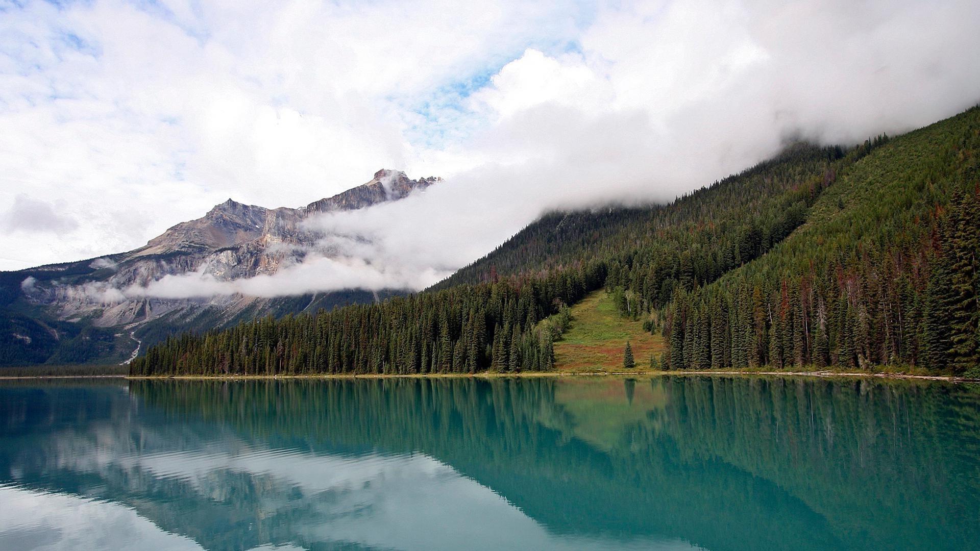 A beautiful lake surrounded by mountains, pine forest and clouds