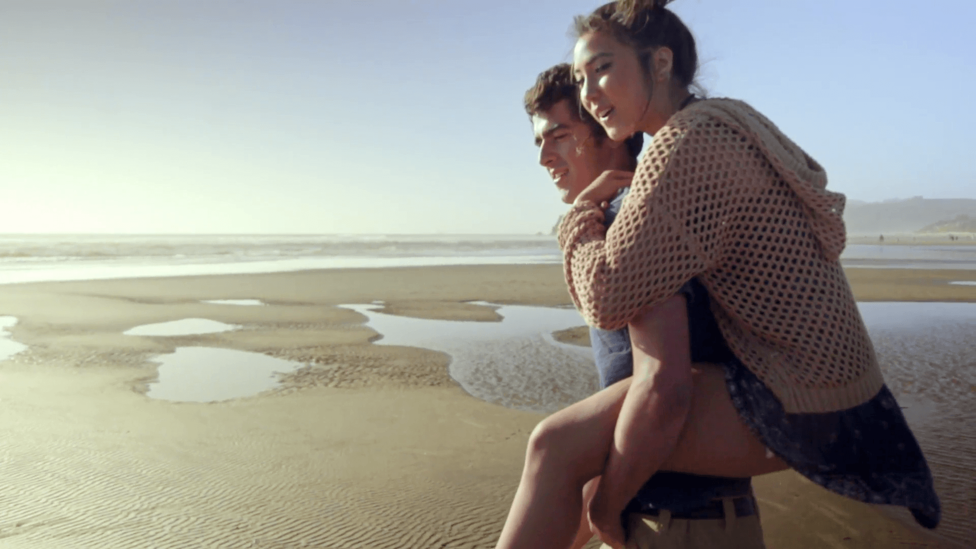 Teenage boy gives his teenage girlfriend a piggyback ride at the beach Stock Video Footage
