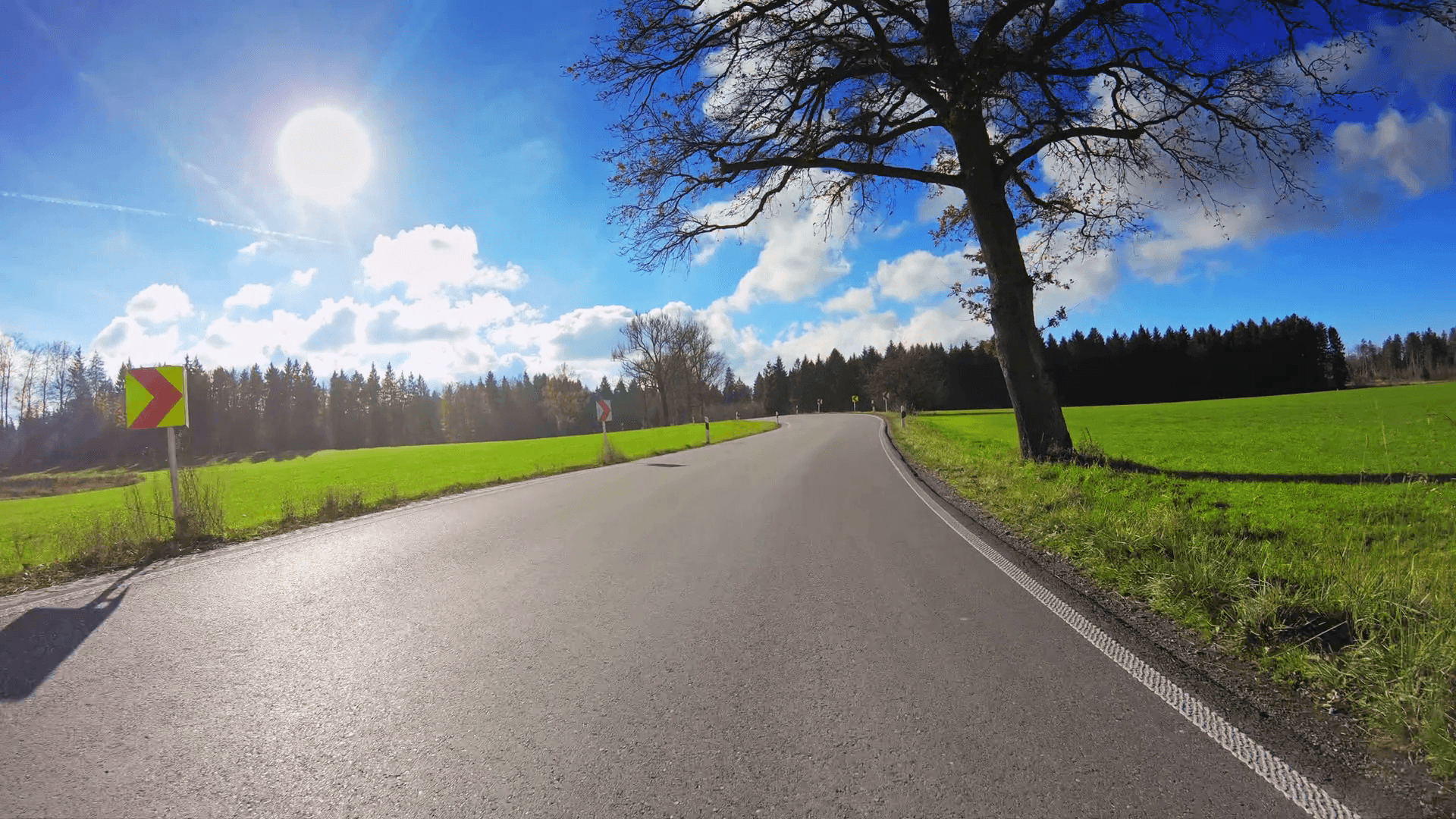 POV vehicle drive across beautiful countryside, local narrow road, green grassland, trees, shining sun blue sky, car travel gopro point of view Stock