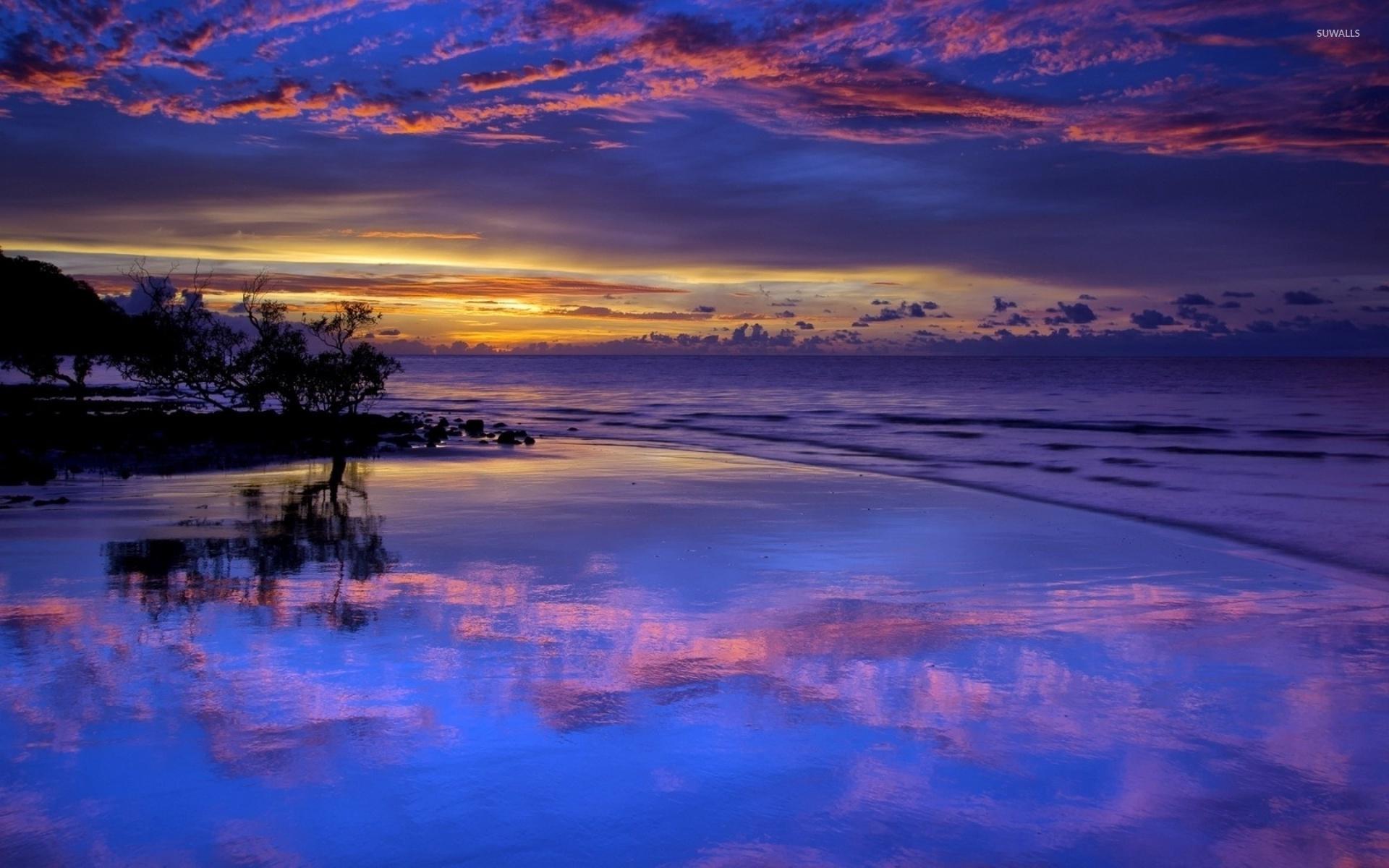 Amazing purple sunset clouds reflected in the wet beach