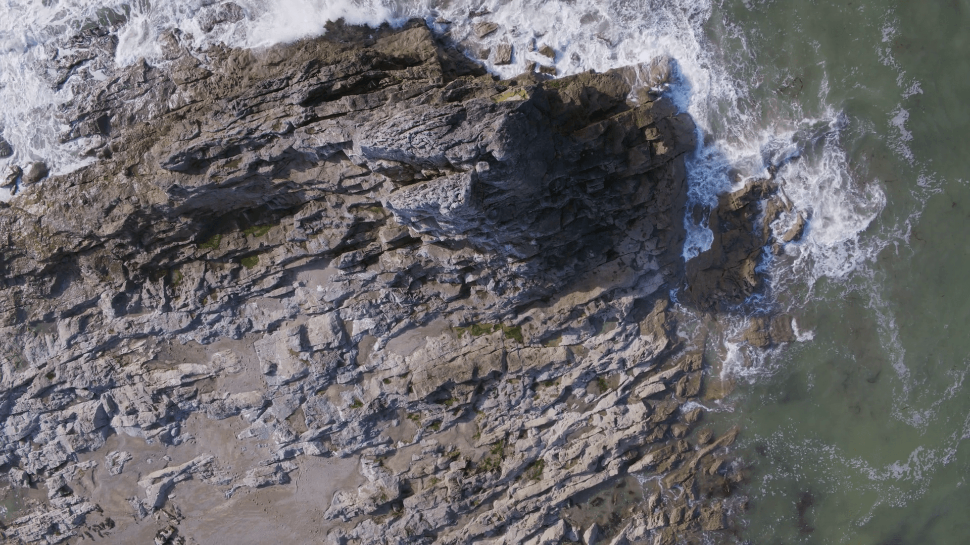 Aerial drone footage of rock formation at beach. Scenic view of sea waves breaking on rocky shore. The video is filmed from an overhead perspective