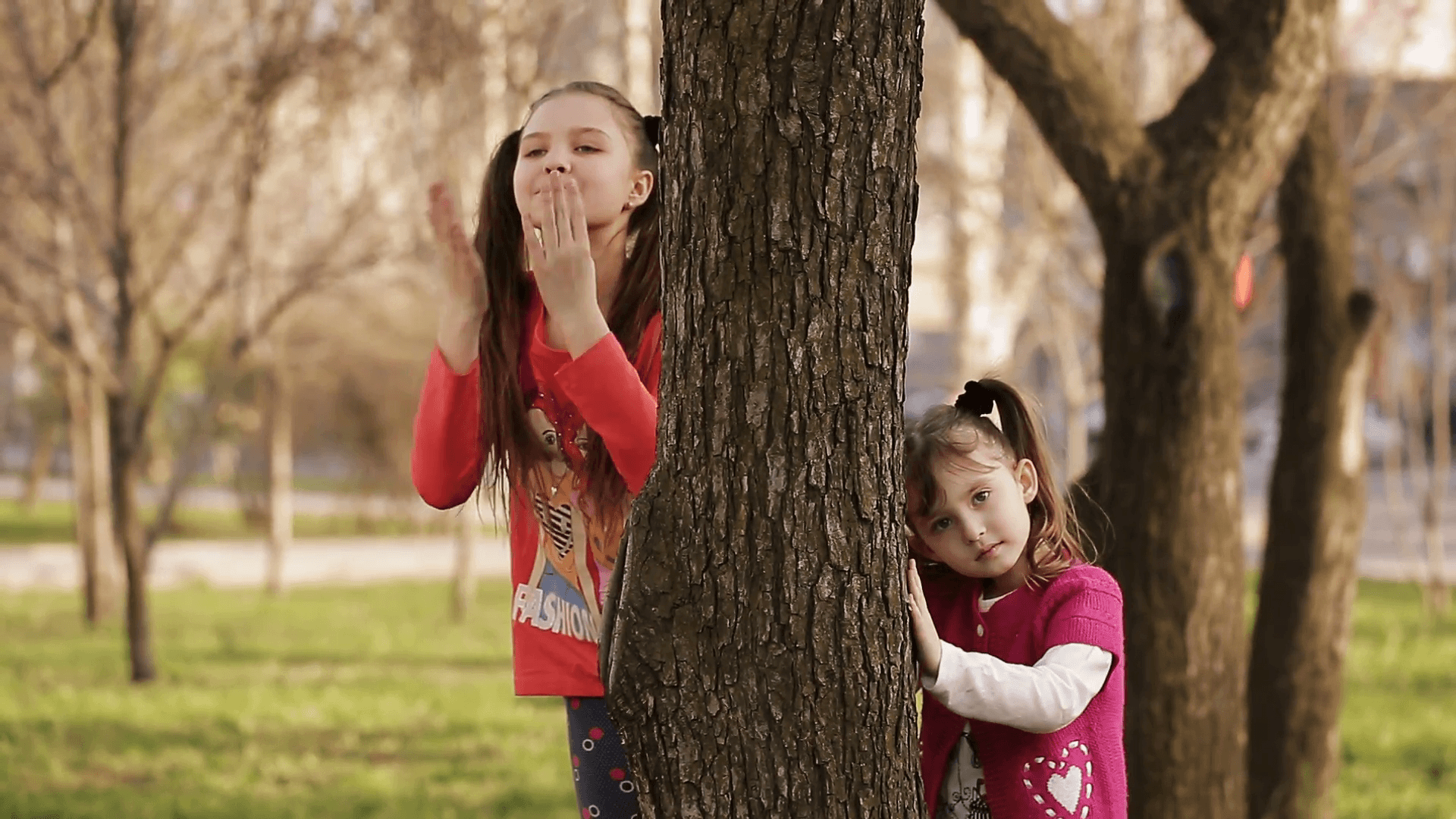 Cheerful girl playing hide and seek behind a tree