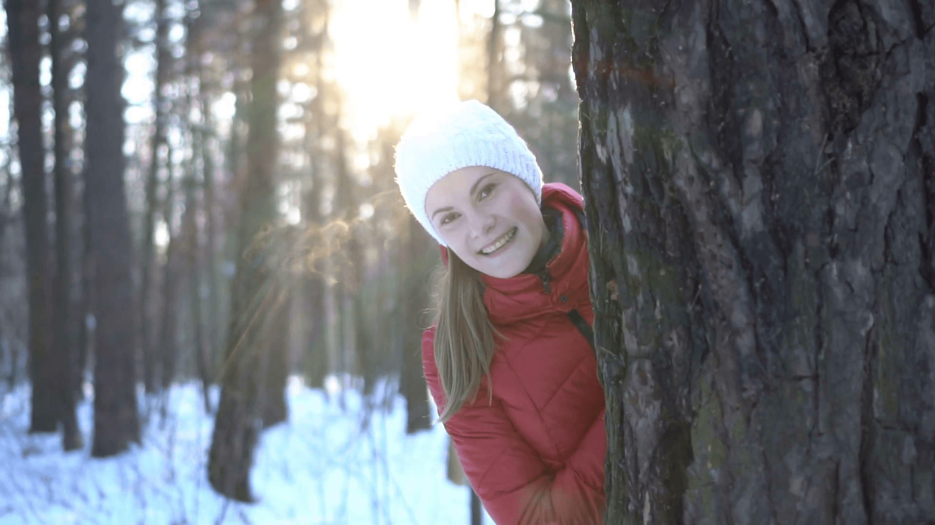 Beautiful young woman in winter park hiding behind the tree, smiling, having fun. Slow motion video Stock Video Footage