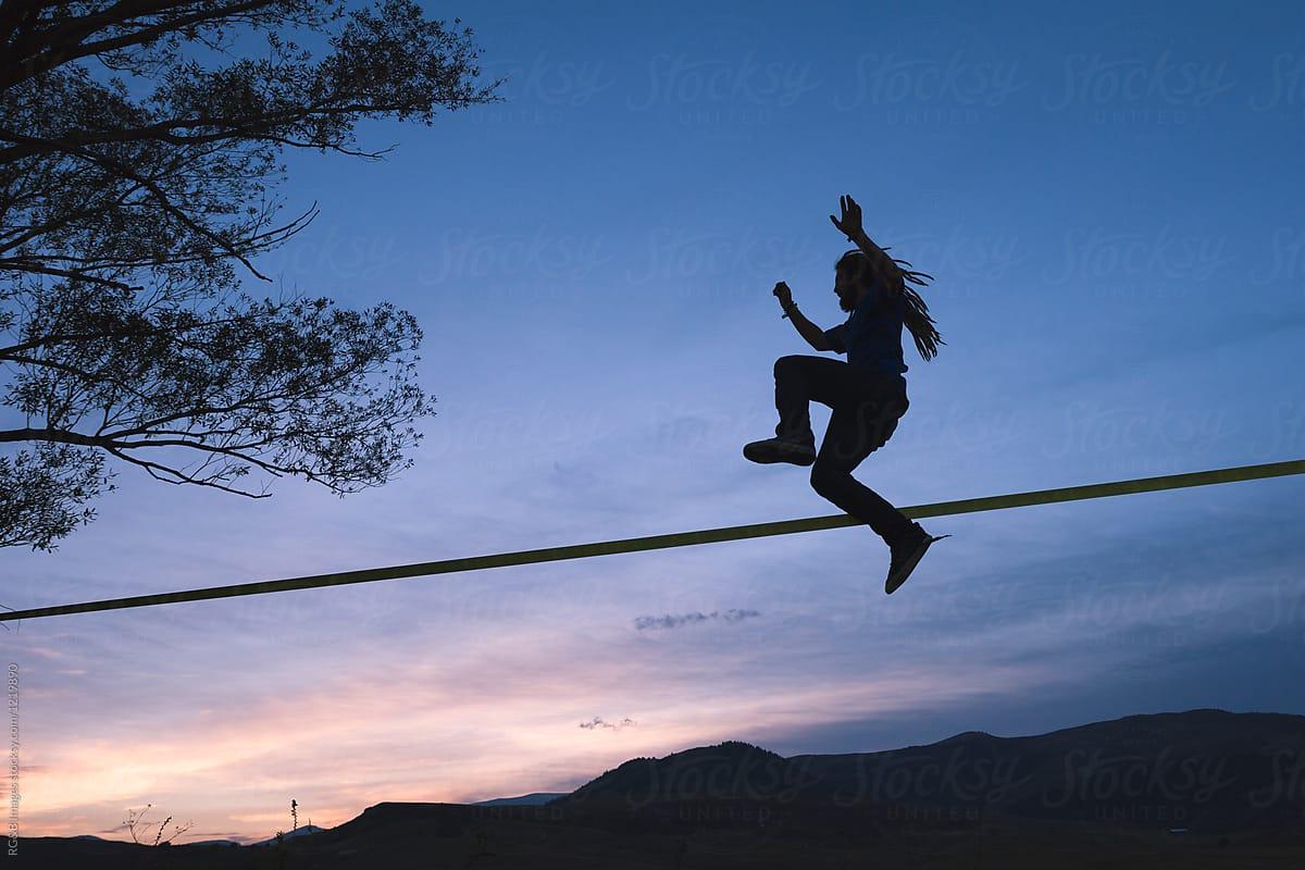 Rebel man with dreads jumping on slackline outdoor during