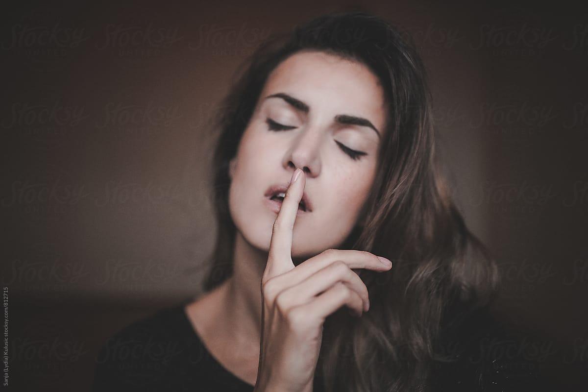 Girl with closed eyes making shhh sign with focus on her