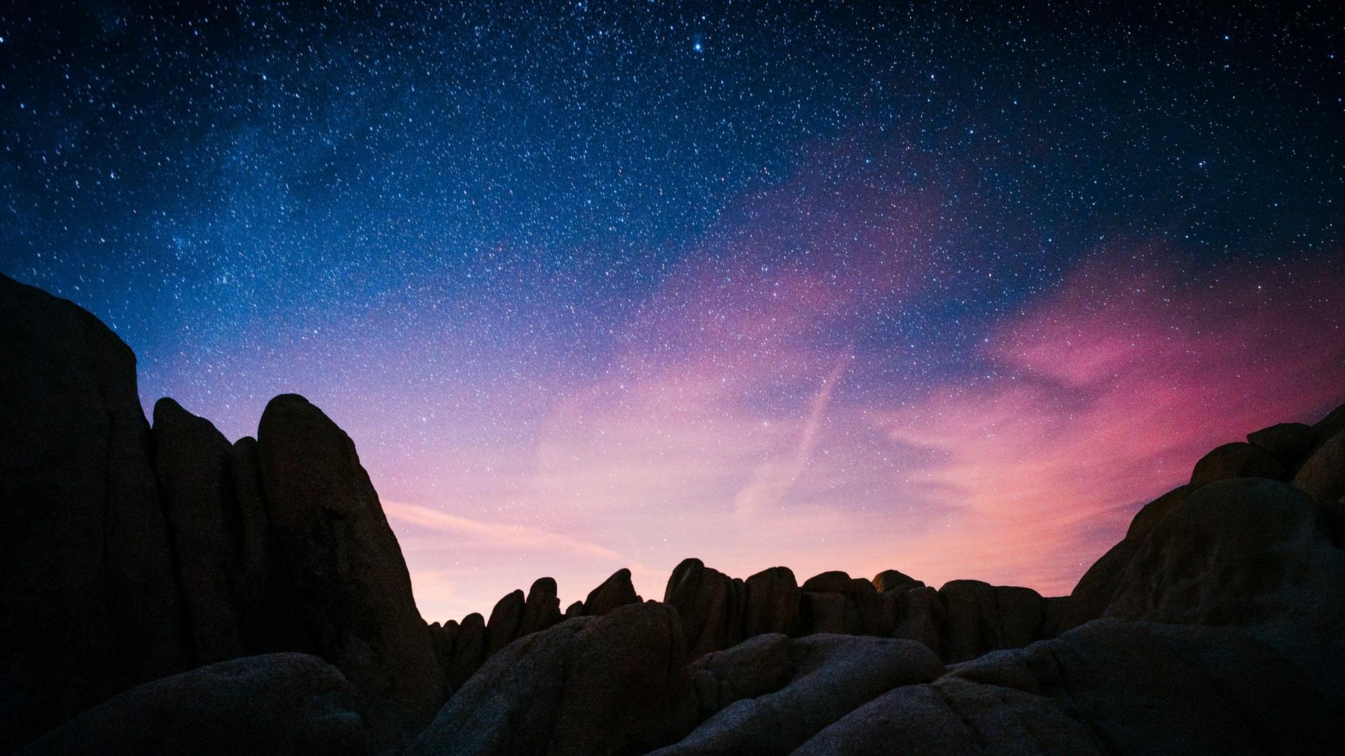 The sky full of stars with blue and pink hues over the rock