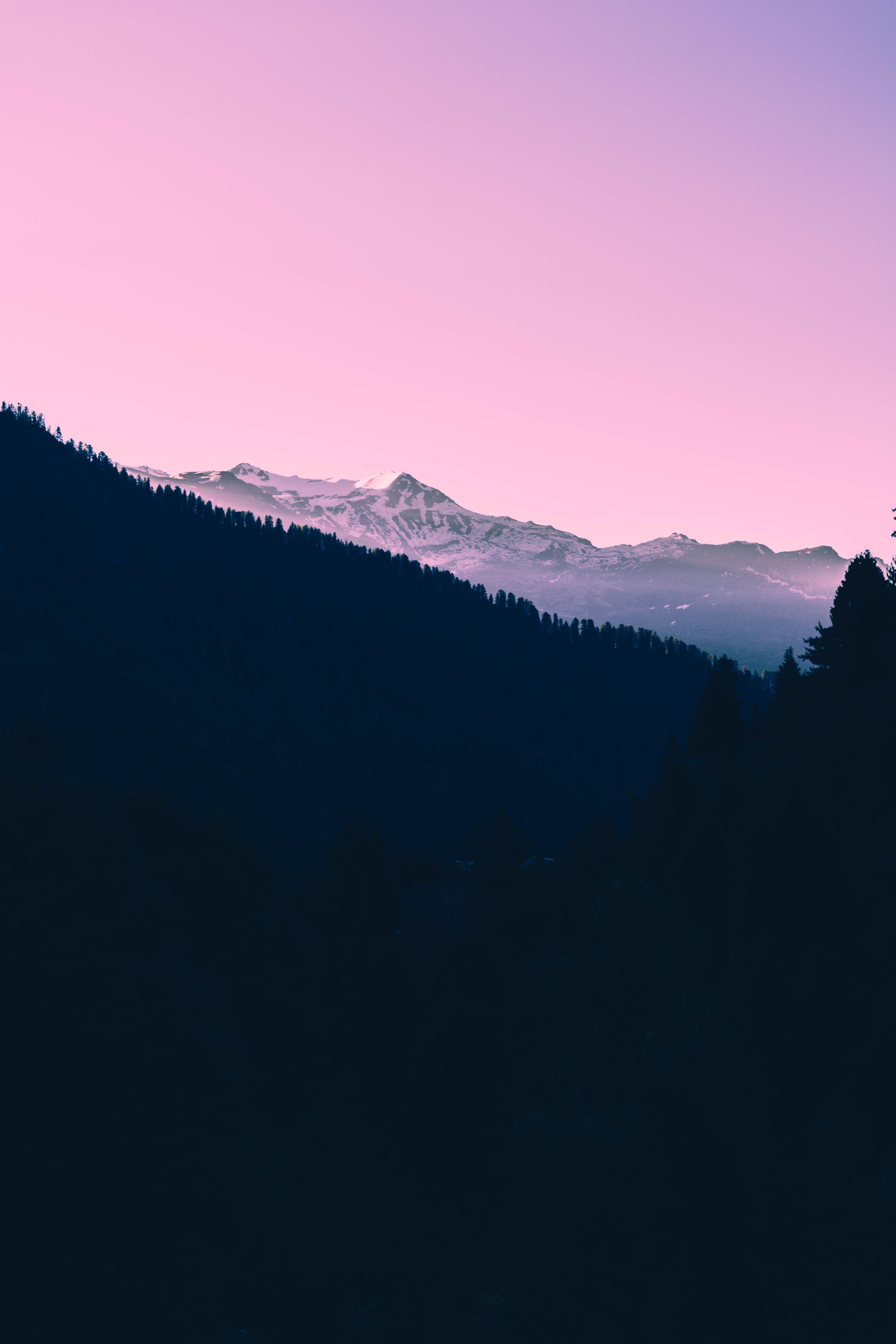 A dark sunset over snow covered mountains and a pink sky