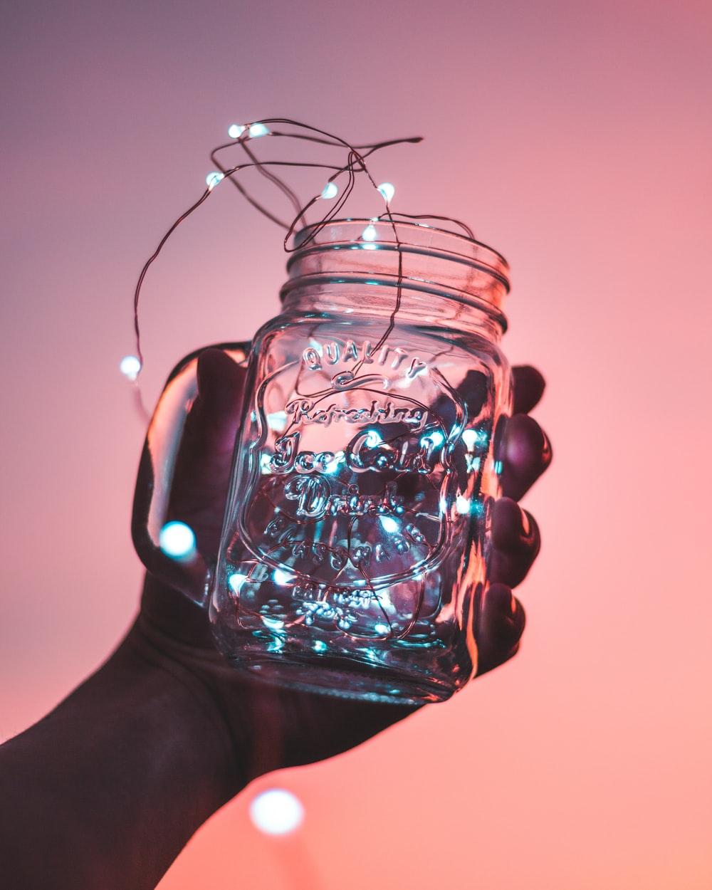 person holding clear glass mason jar with strip lights