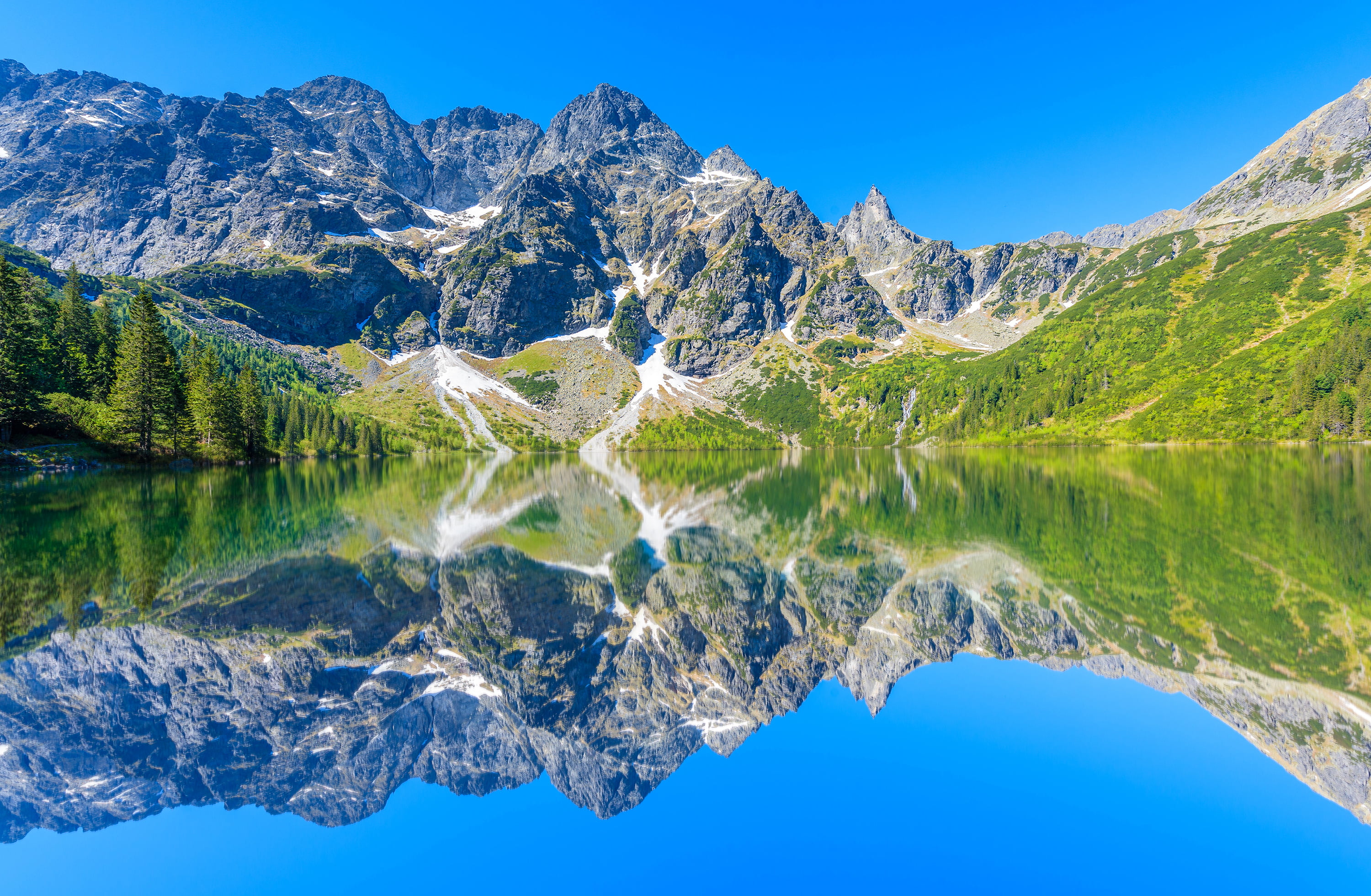 Grey rocky mountains near lake under blue sky HD wallpaper