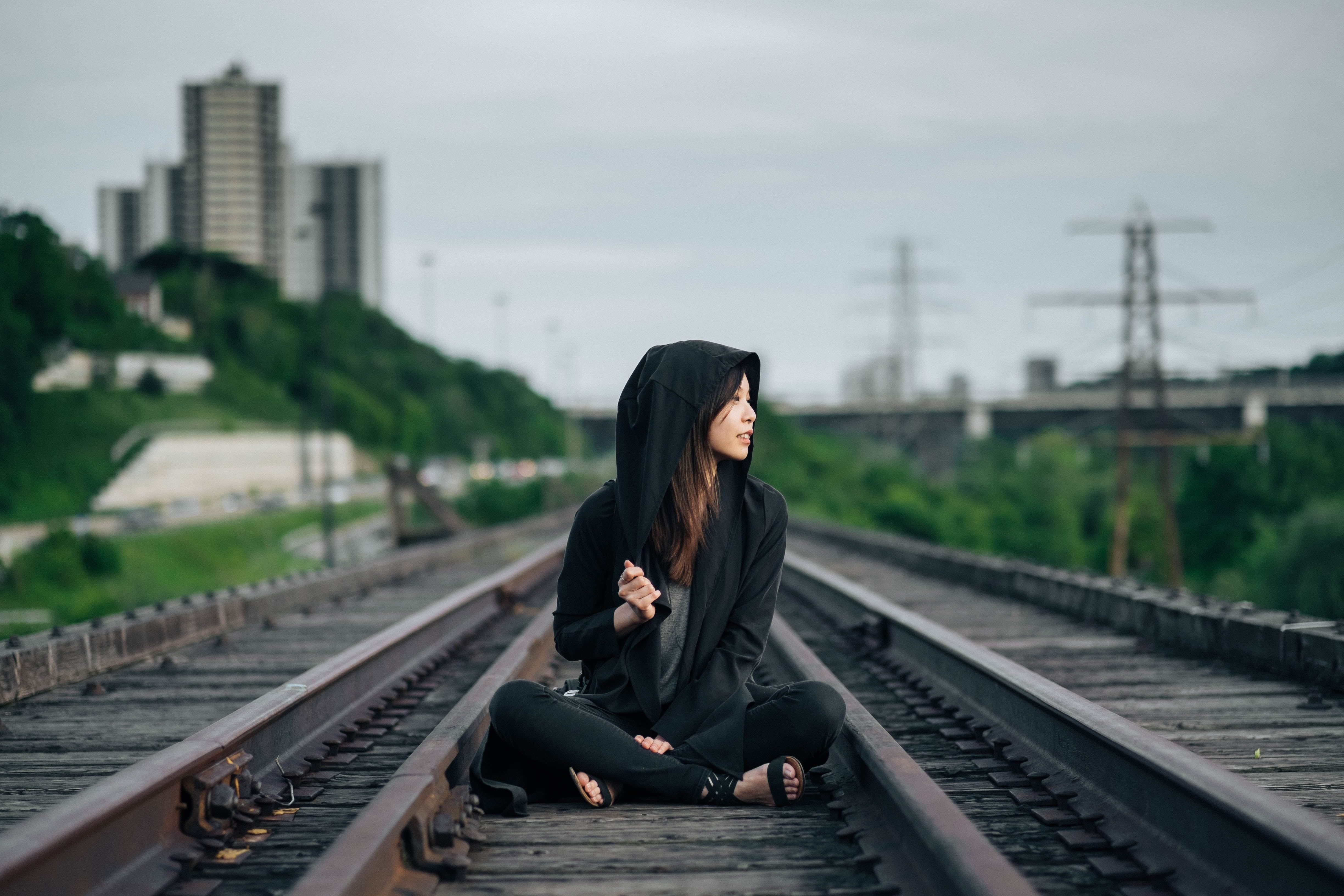 Selective focus photography of woman in black hoodie and pants sitting on train track HD wallpaper