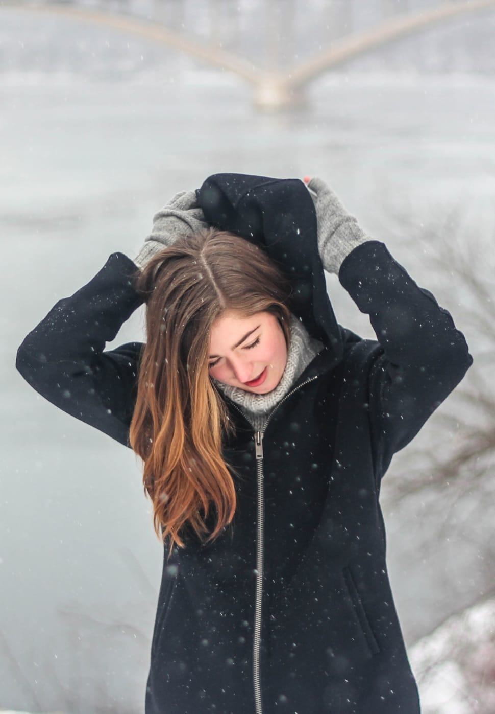 woman in black zip hoodie standing in a snow filled field during