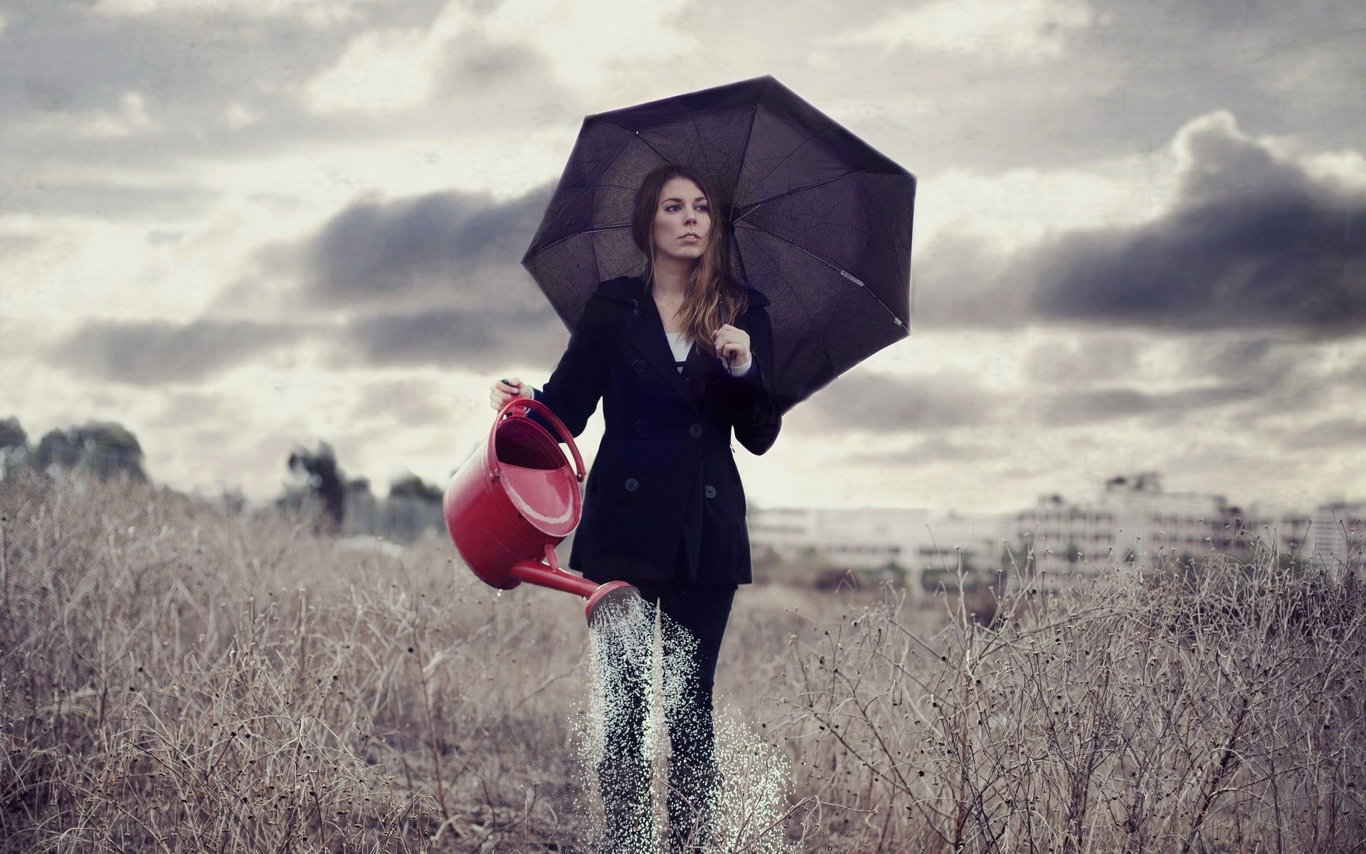 Photo of woman walking on field holding umbrella and watering can