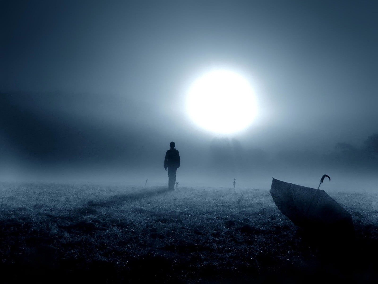Man walking on grass field with open umbrella under full moon