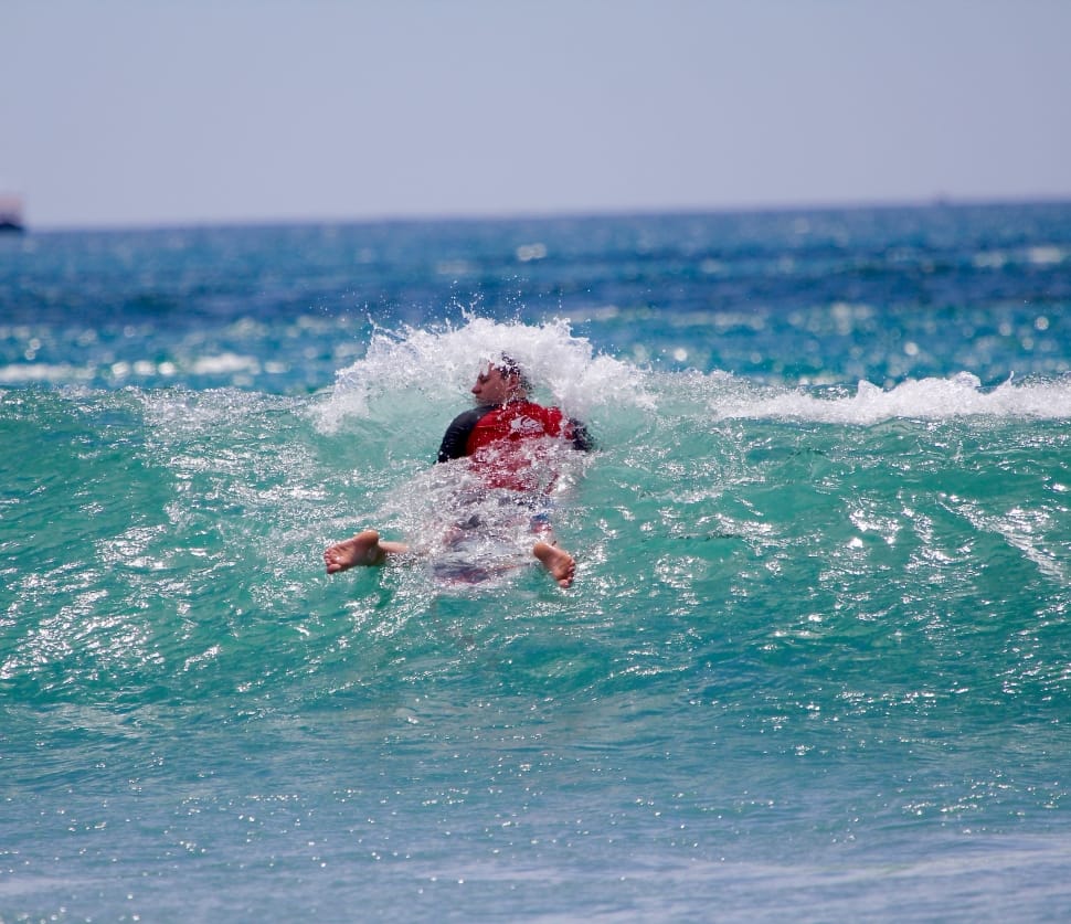 man in red and black shorty wetsuit riding on bodyboard on body