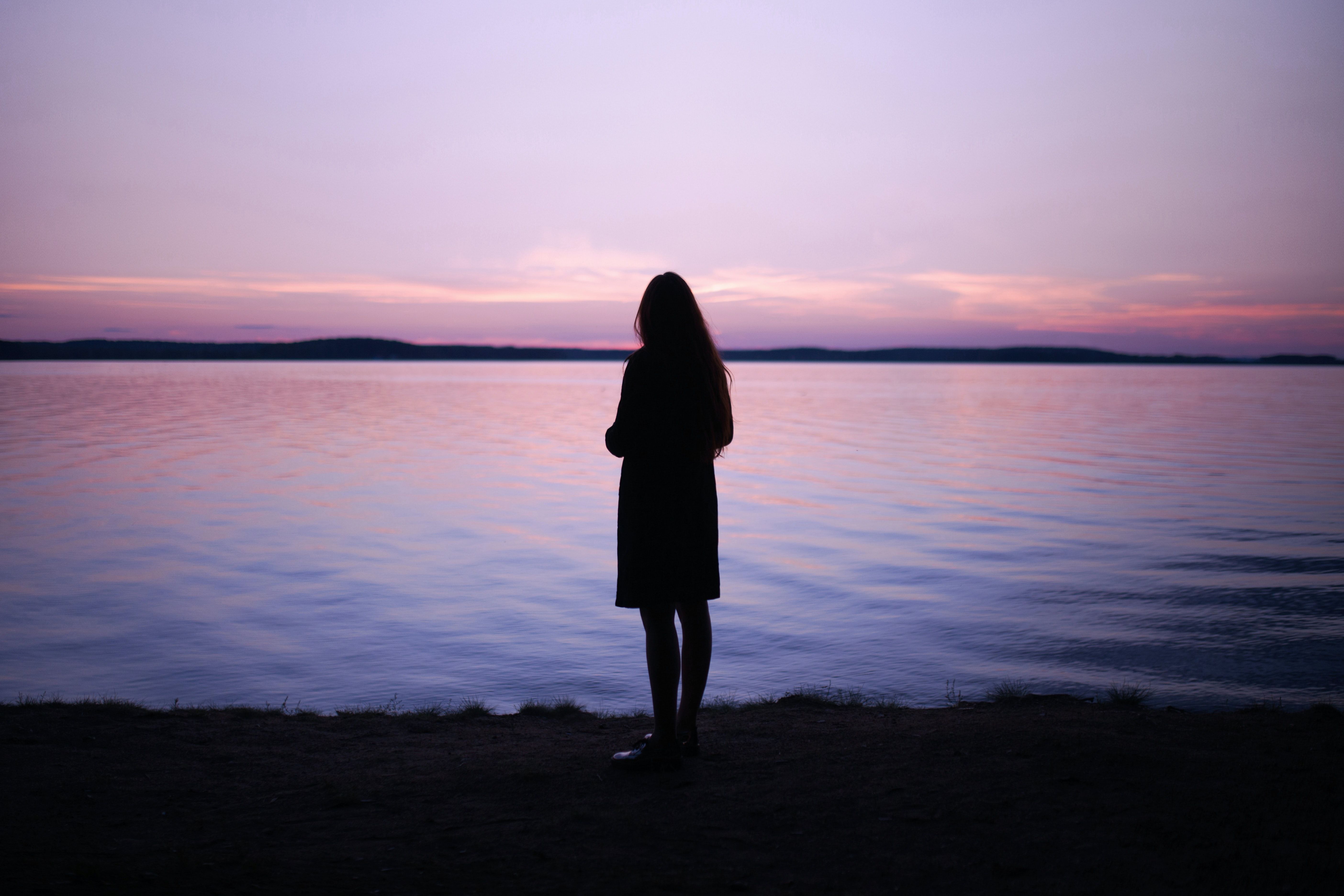 woman standing near body of water during golden hour photo