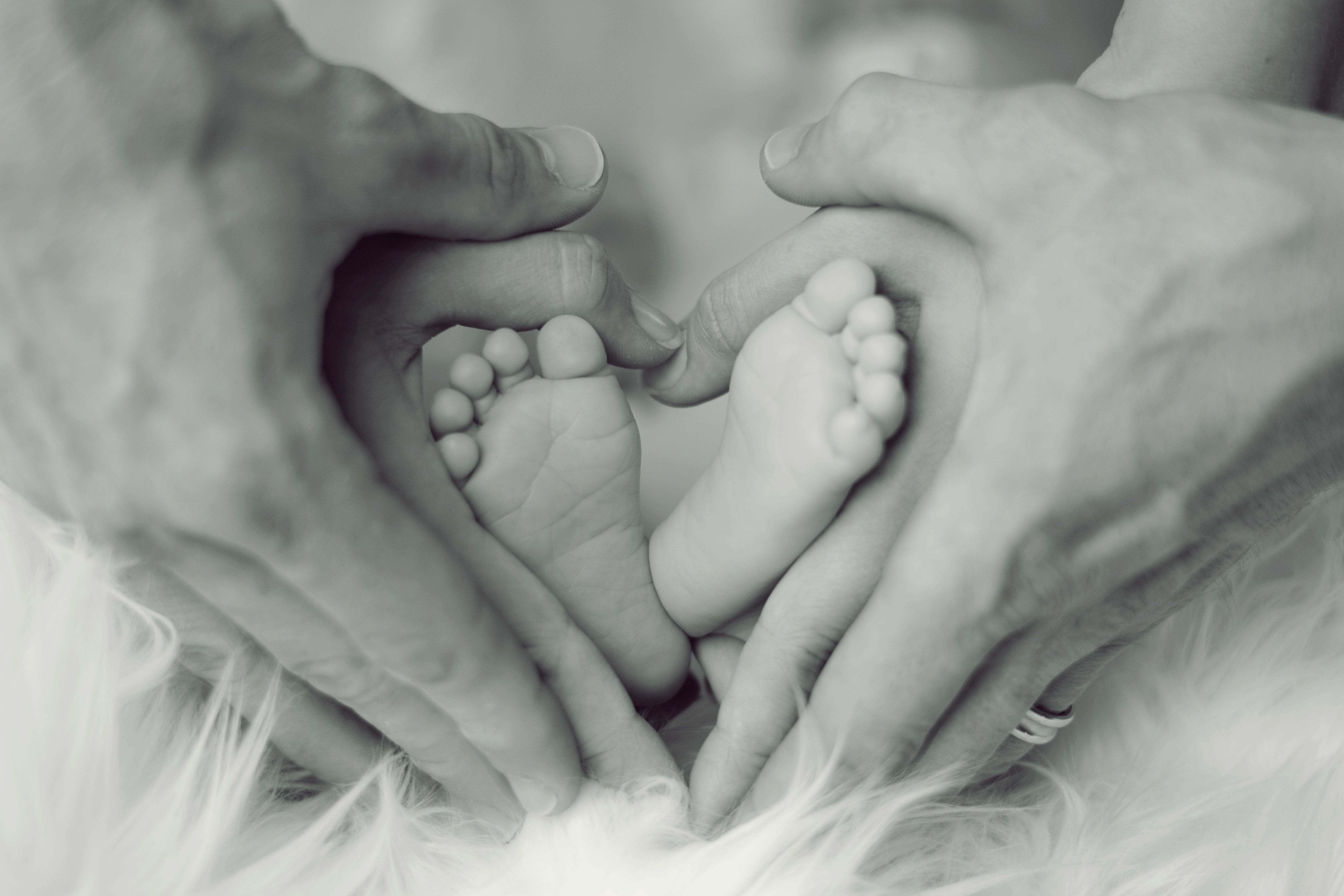 Grayscale Photo of Baby Feet With Father and Mother Hands in Heart