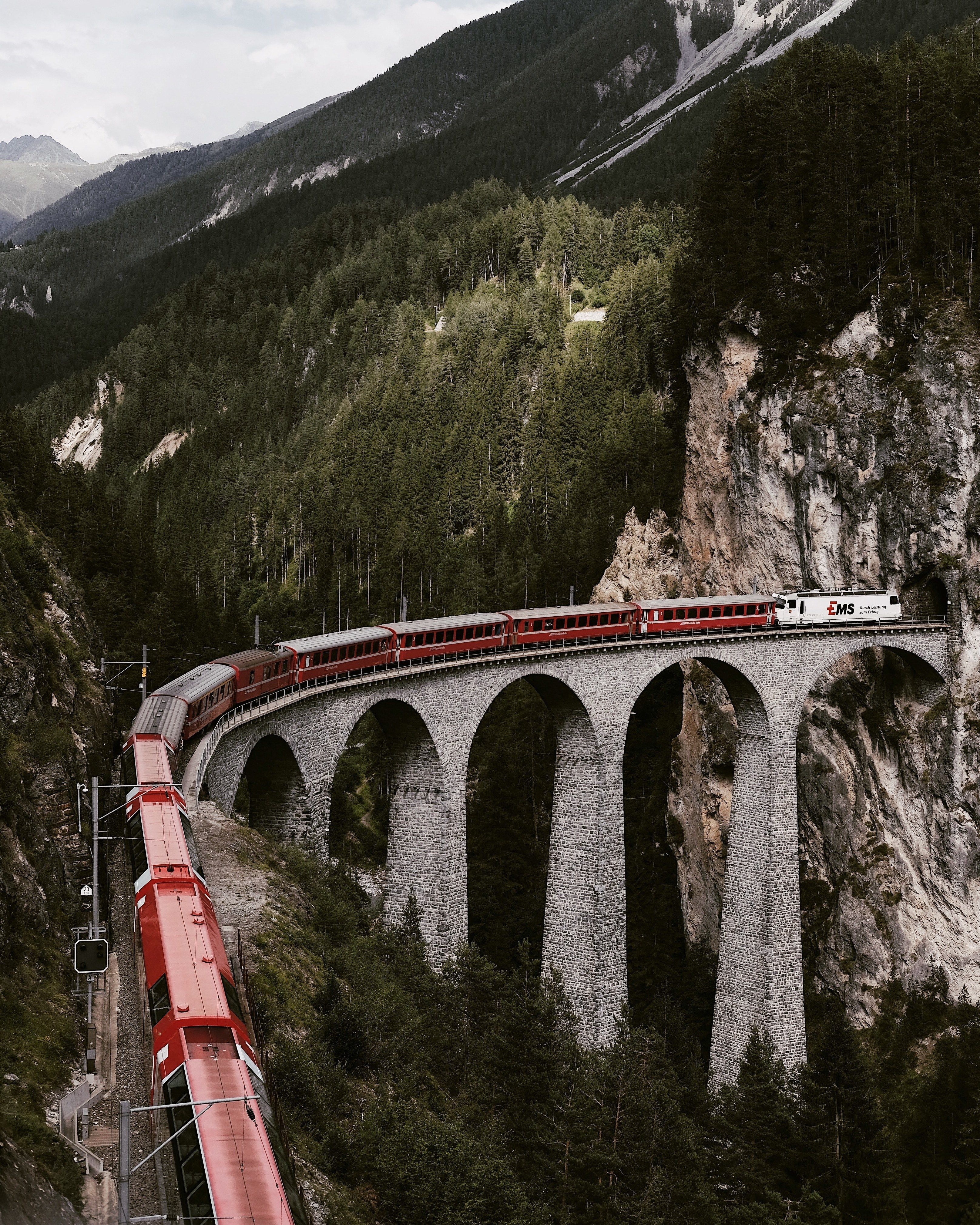 landscape of mountains with a large bridge and red and white train