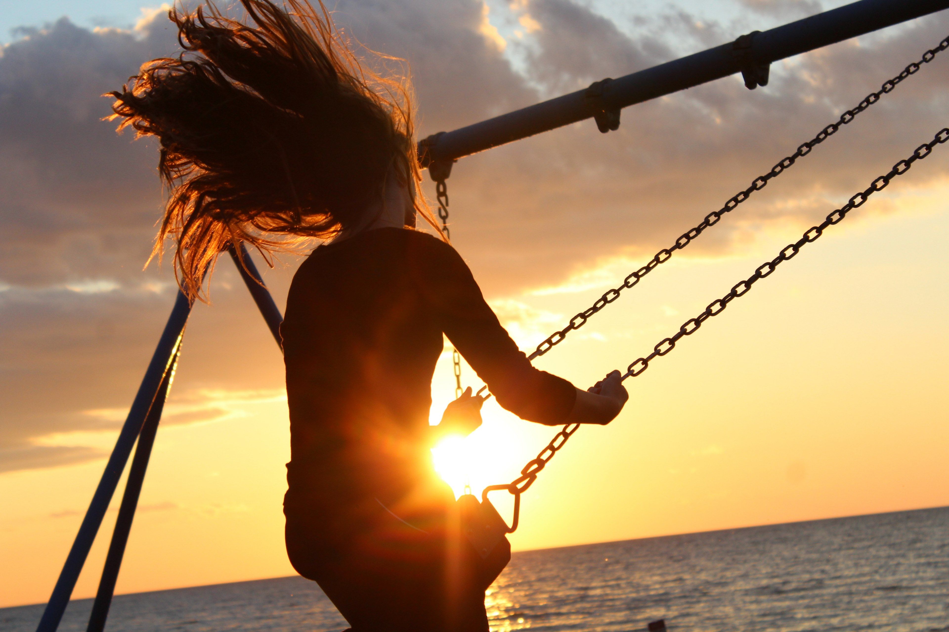 a woman with long hair swings high on a swing near the ocean at