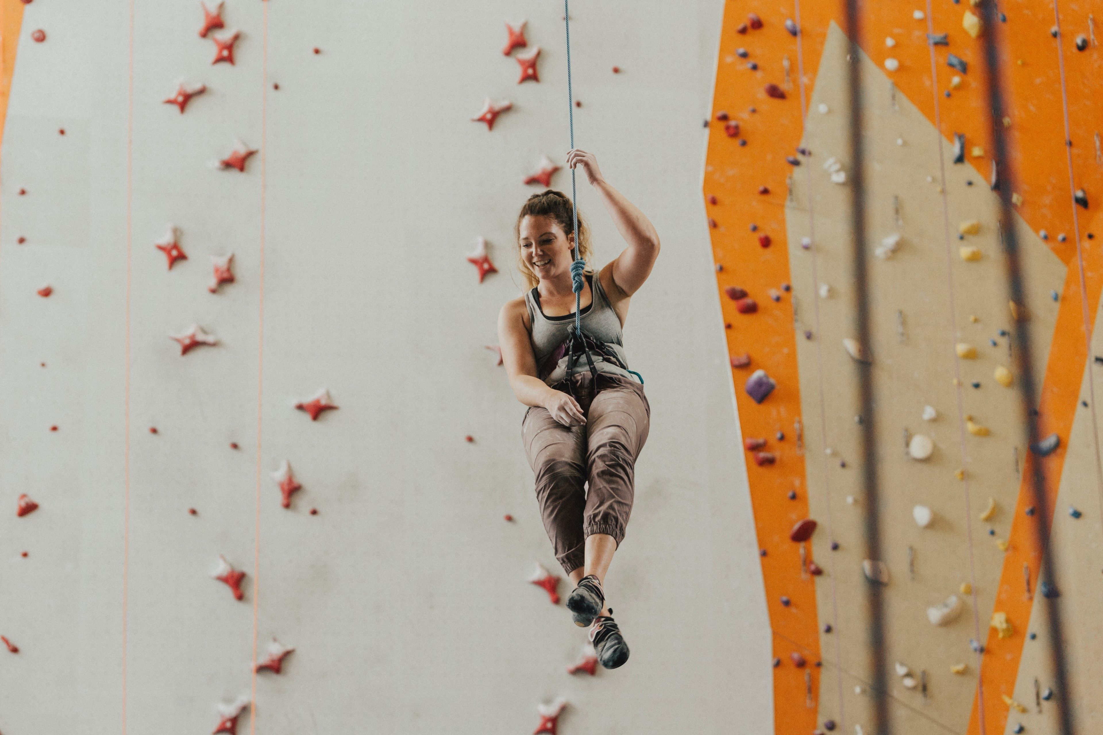 a woman suspended on a rope in front of a climbing wall at stone