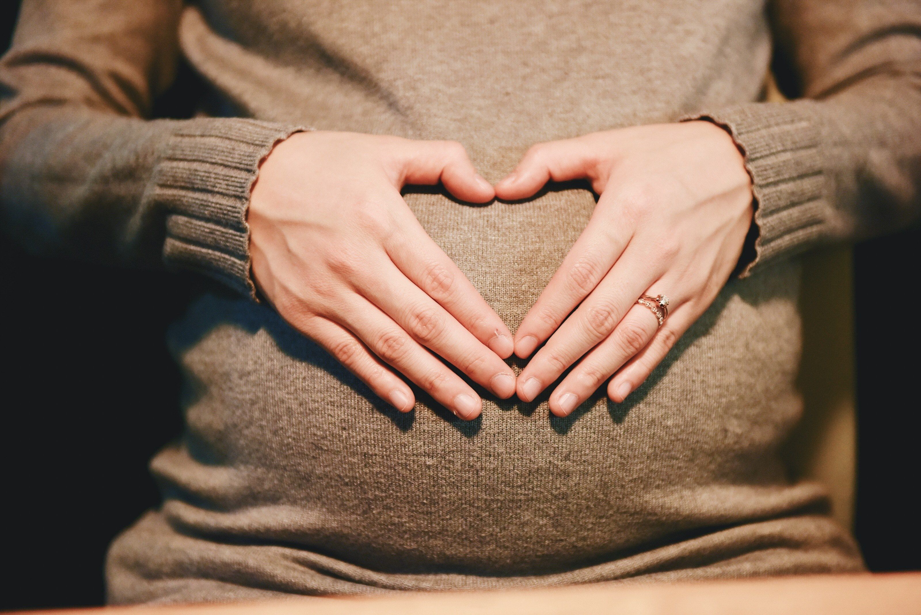 a pregnant woman in a sweater forming a heart with her hands