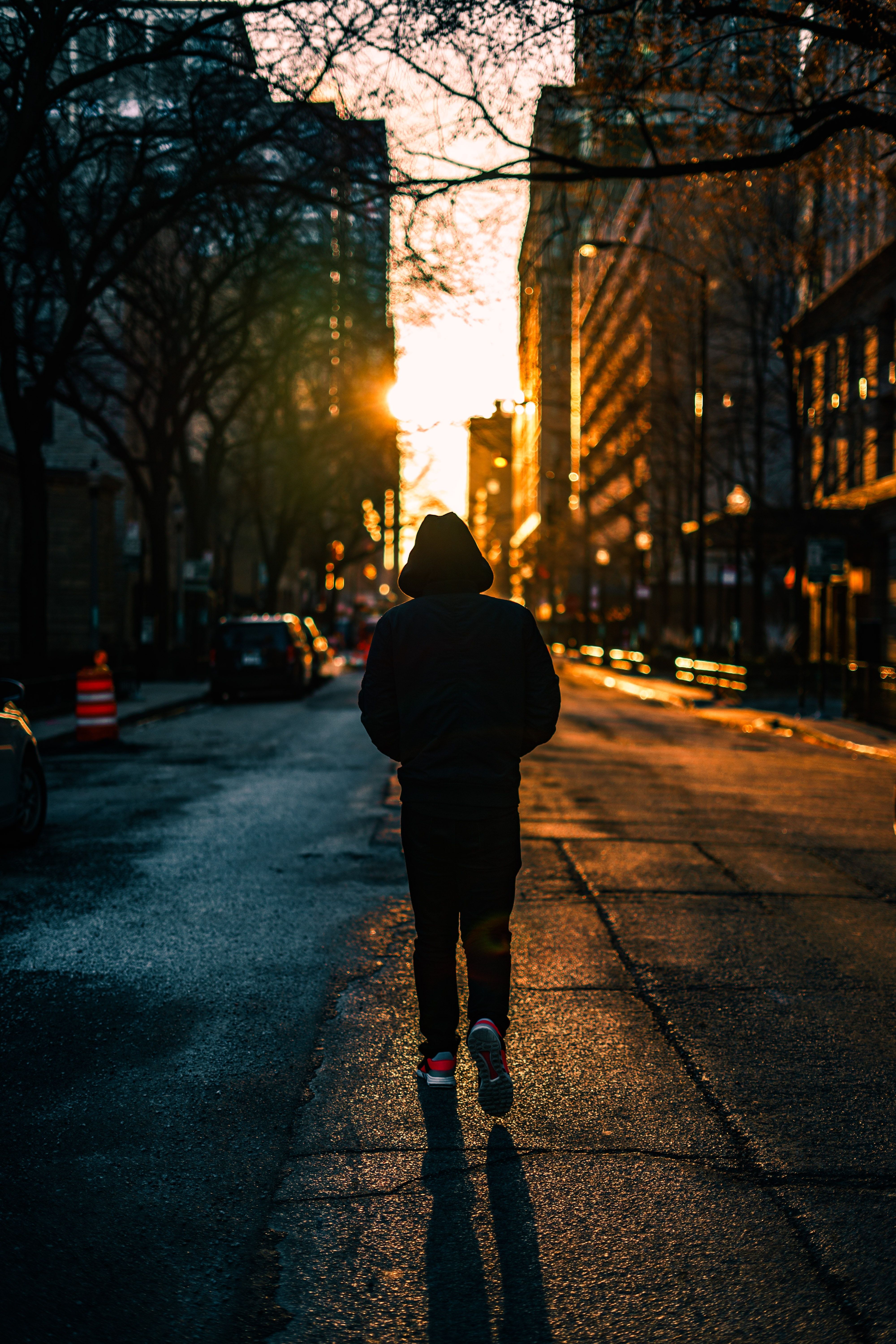 person in black hoodie walking on street during golden hour photo