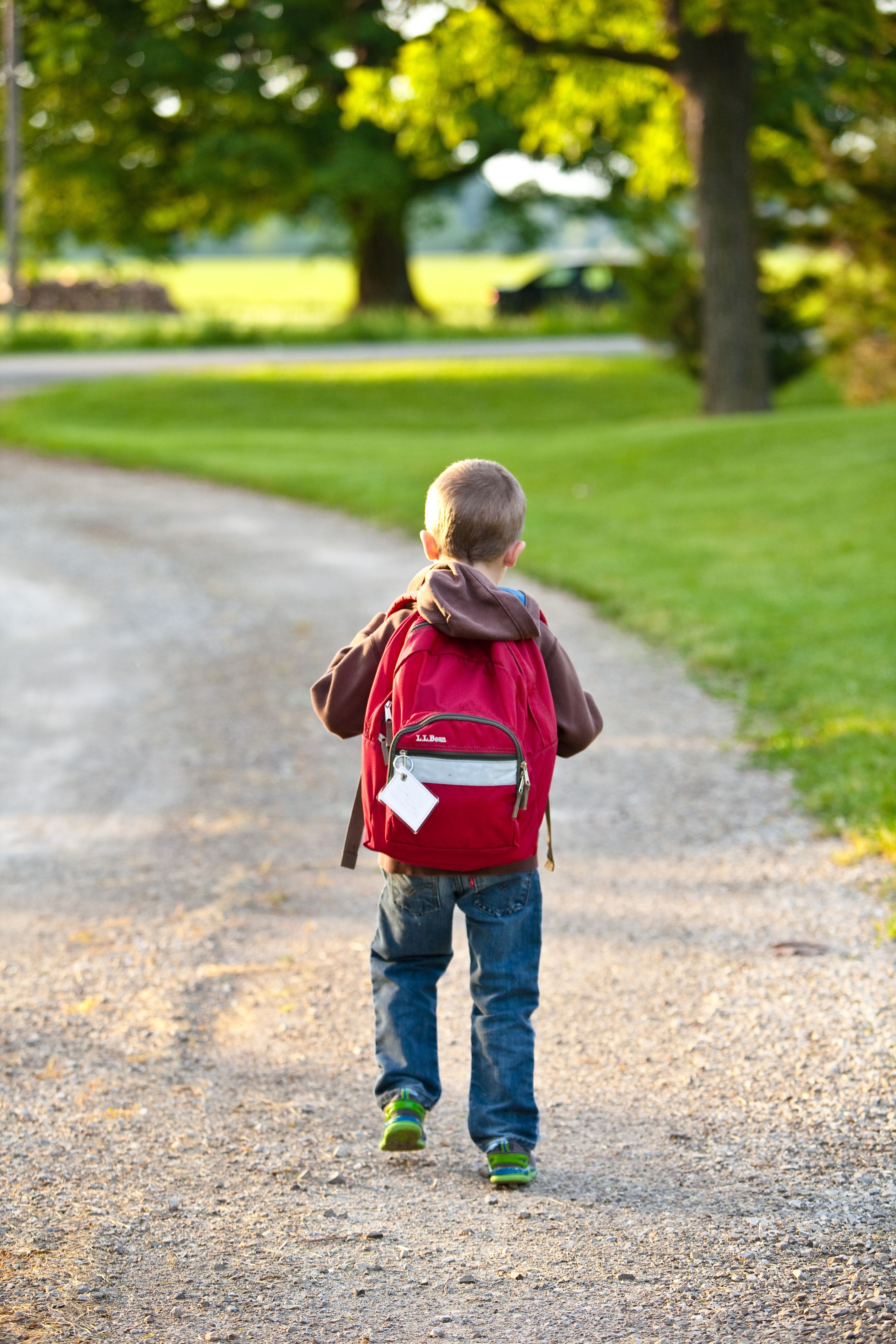 Boy in Brown Hoodie Carrying Red Backpack While Walking on Dirt