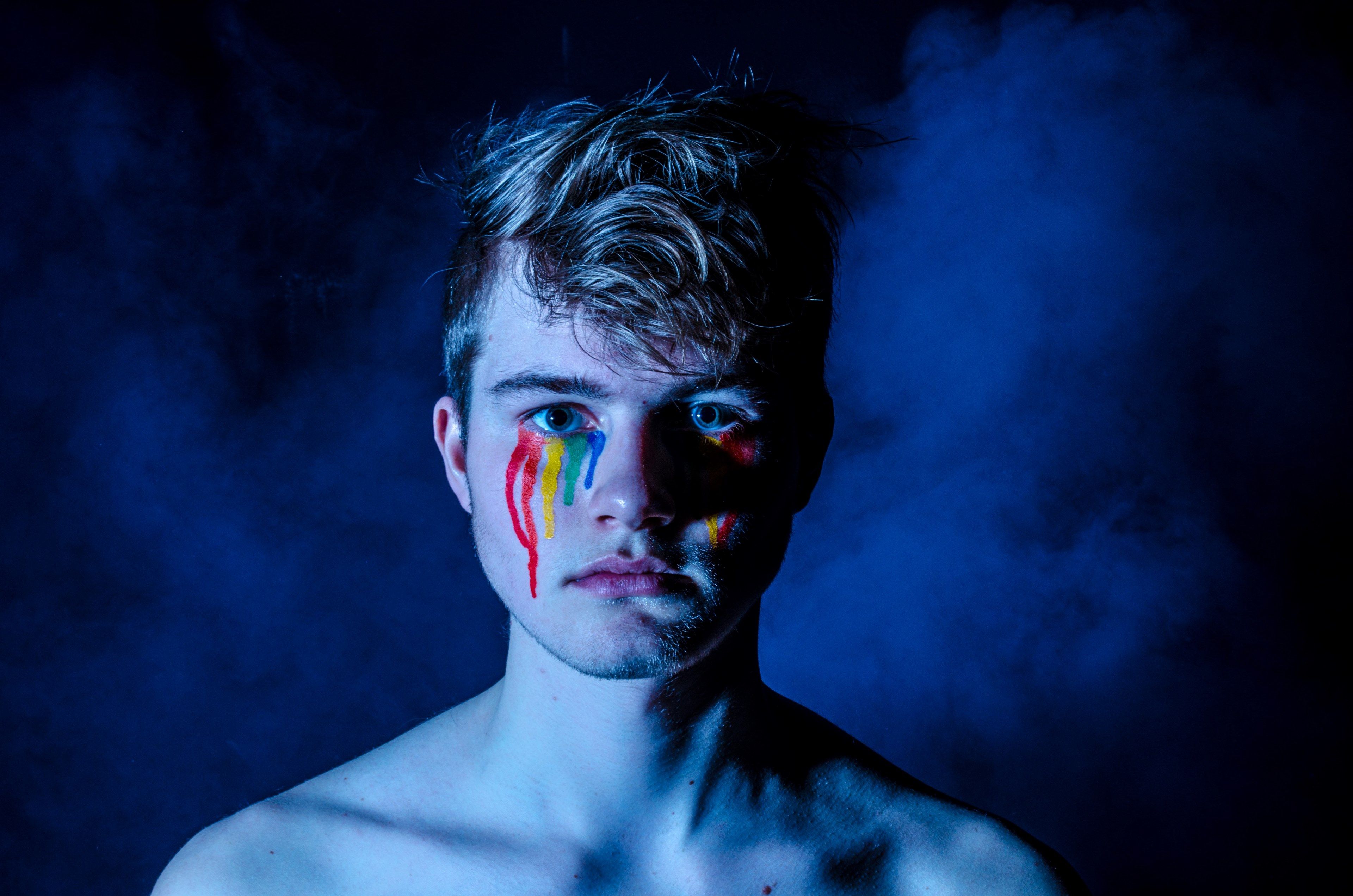 young man with rainbow lgbt face pain in dark smoketears