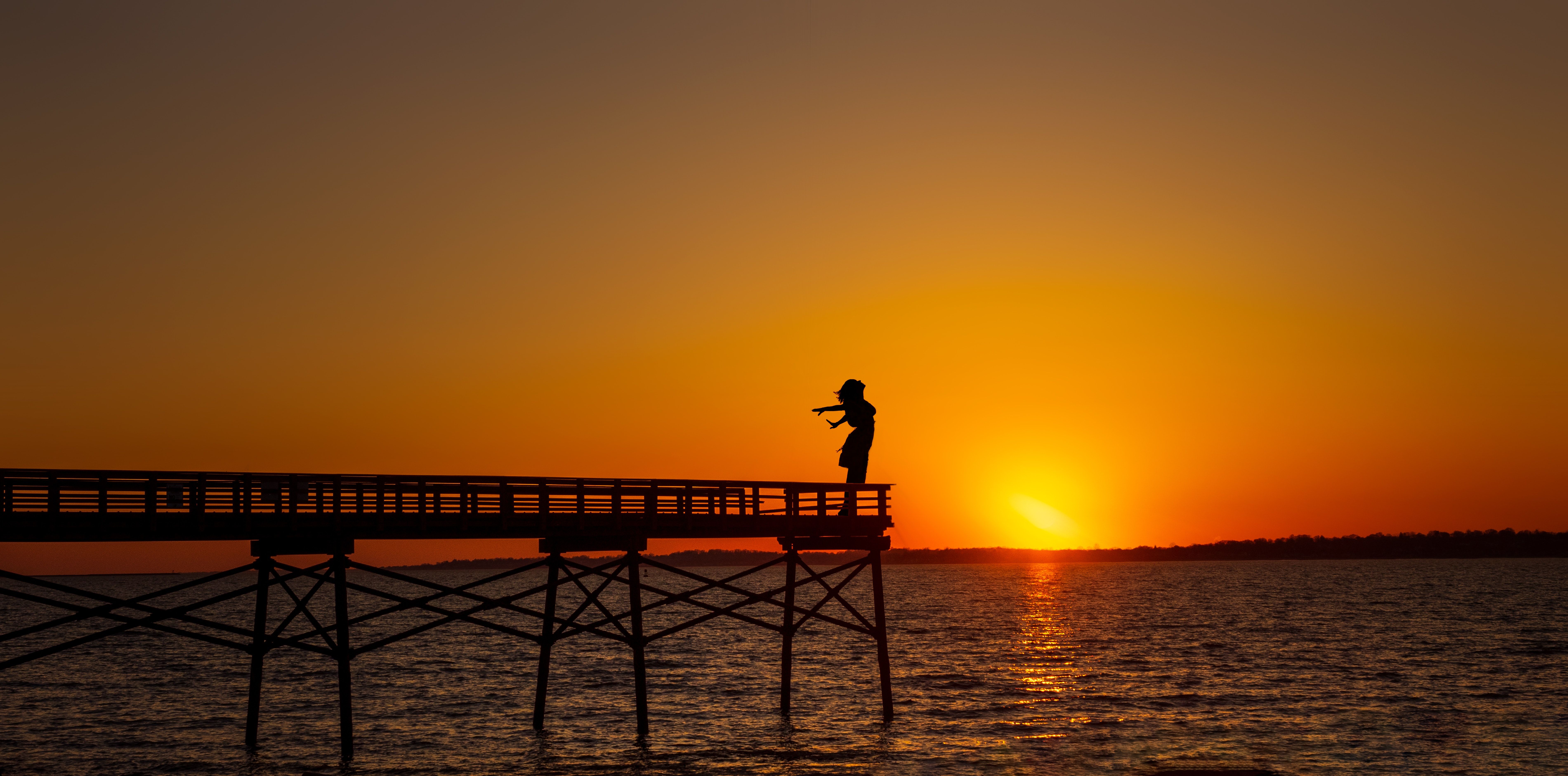 Silhouette Of Woman Standing On Dock During Sunset · Free