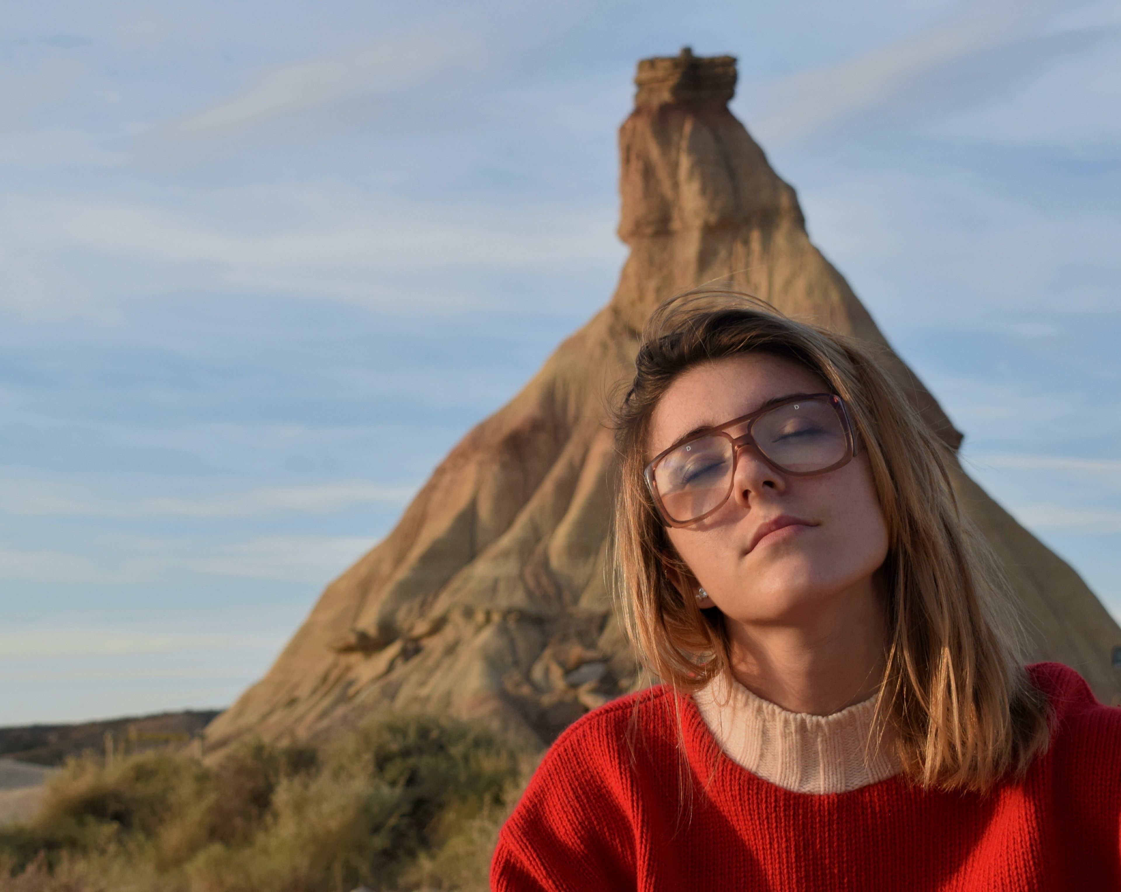 a woman wearing glasses and a red sweater sitting in front of bardenas realeswoman in nature 4k wallpaper and background