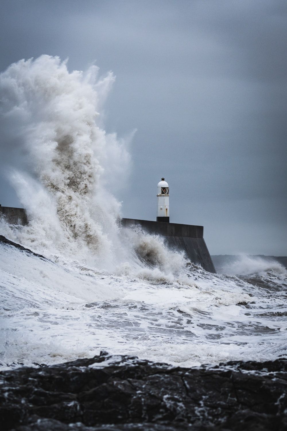 big waves crashing on lighthouse during daytime photo