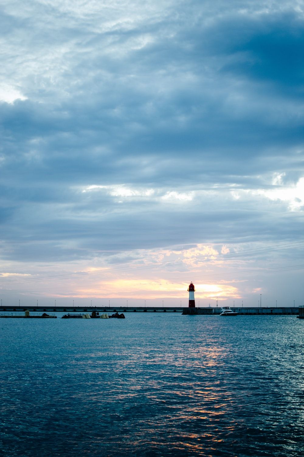 silhouette of lighthouse on sea dock under cloudy sky during