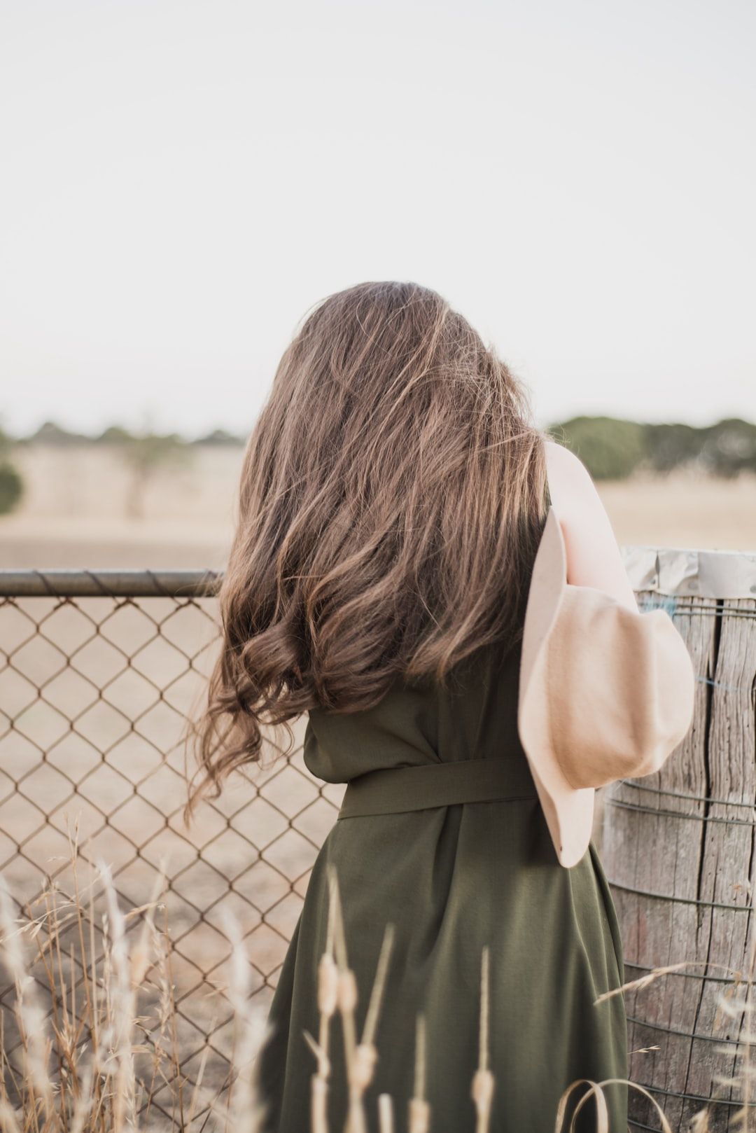 Woman Wearing Green Sleeveless Dress Standing Next To Chain Link Fence During Daytime Photo