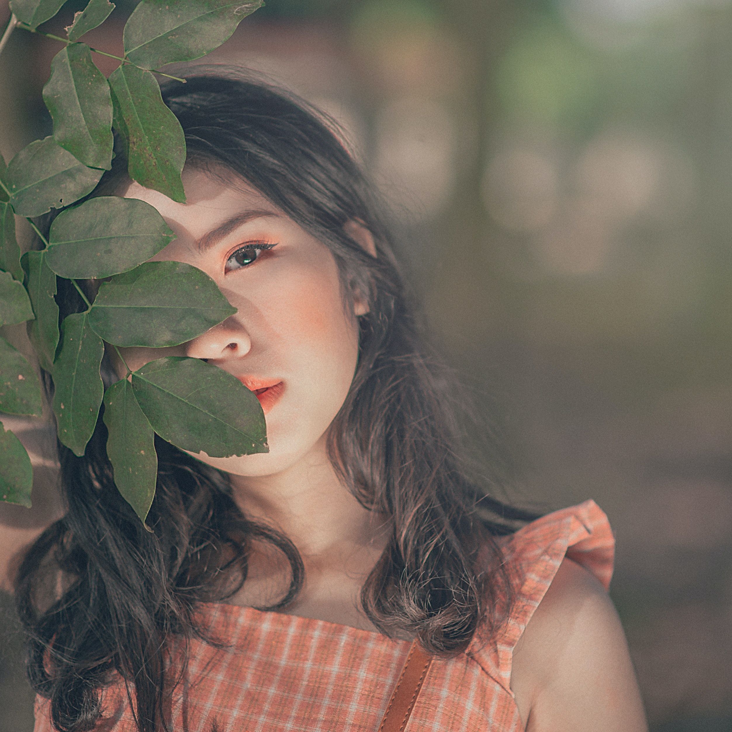 Selective Focus Photography of Woman in Orange Sleeveless Top Hiding Face Behind Tree's Leaf · Free