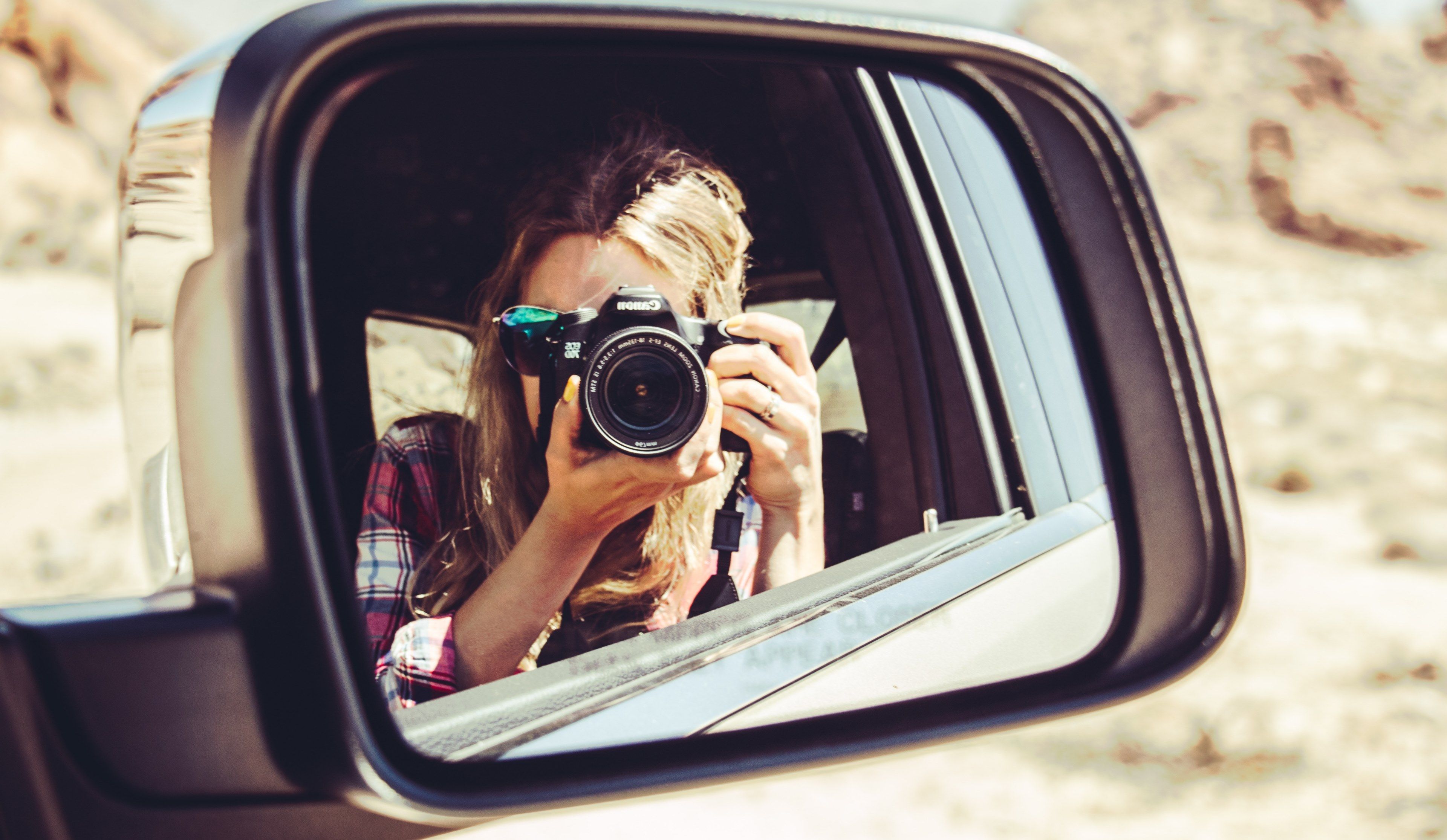 Wallpaper / a blonde woman in pink plaid taking a photo of herself by pointing a canon camera at a sideview mirror, side view mirror selfie 4k wallpaper