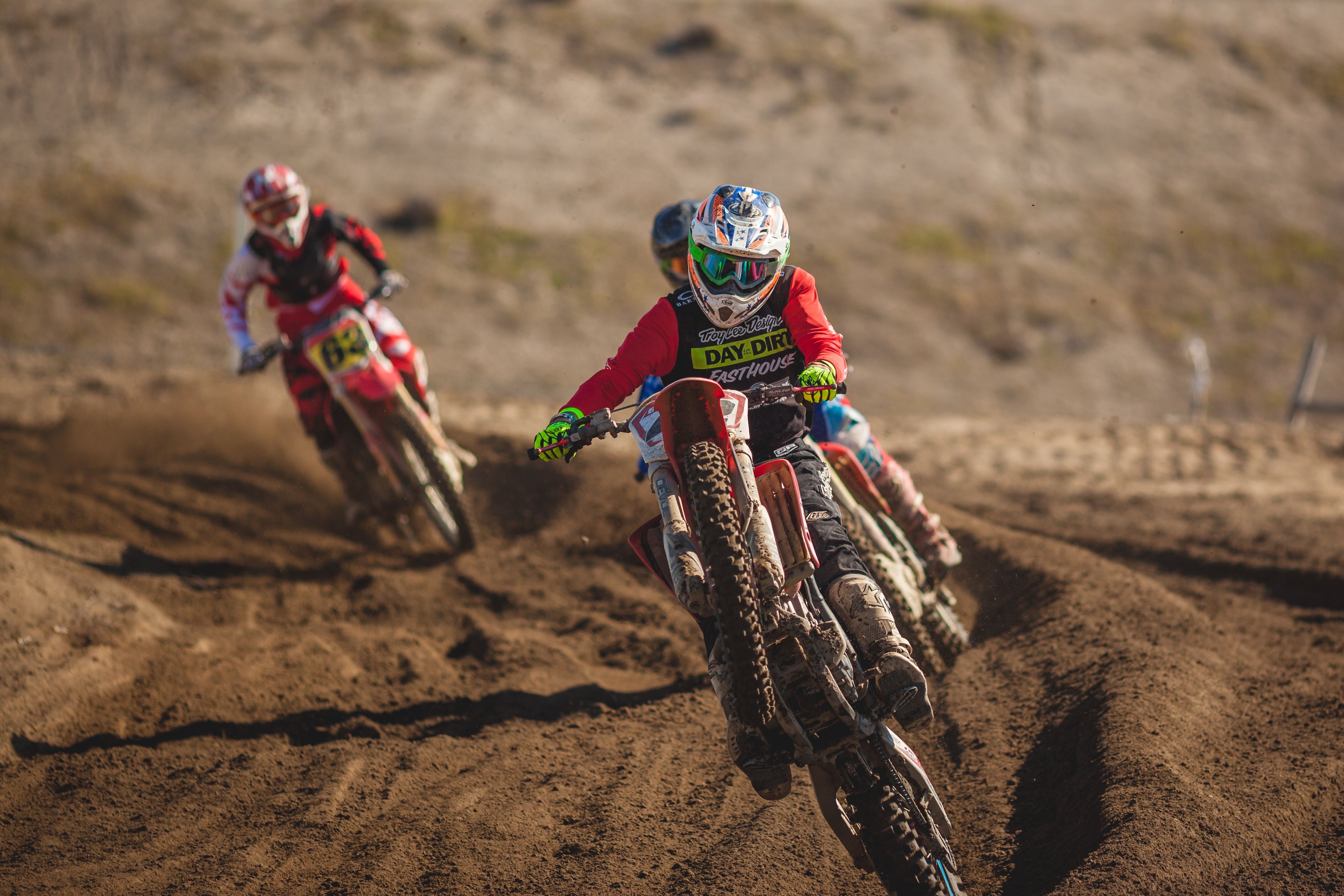 motocross rider doing wheelie on a dirt bike on race track in front of two other motocross racers during daytime free image