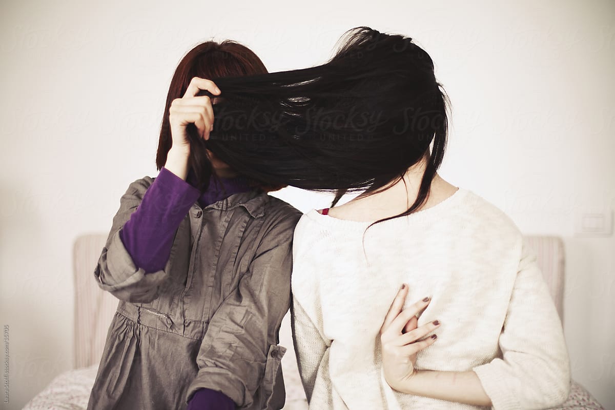 Two girls, one hiding her face with hair, the other seen from the back while sitting on bed by Laura Stolfi, Face