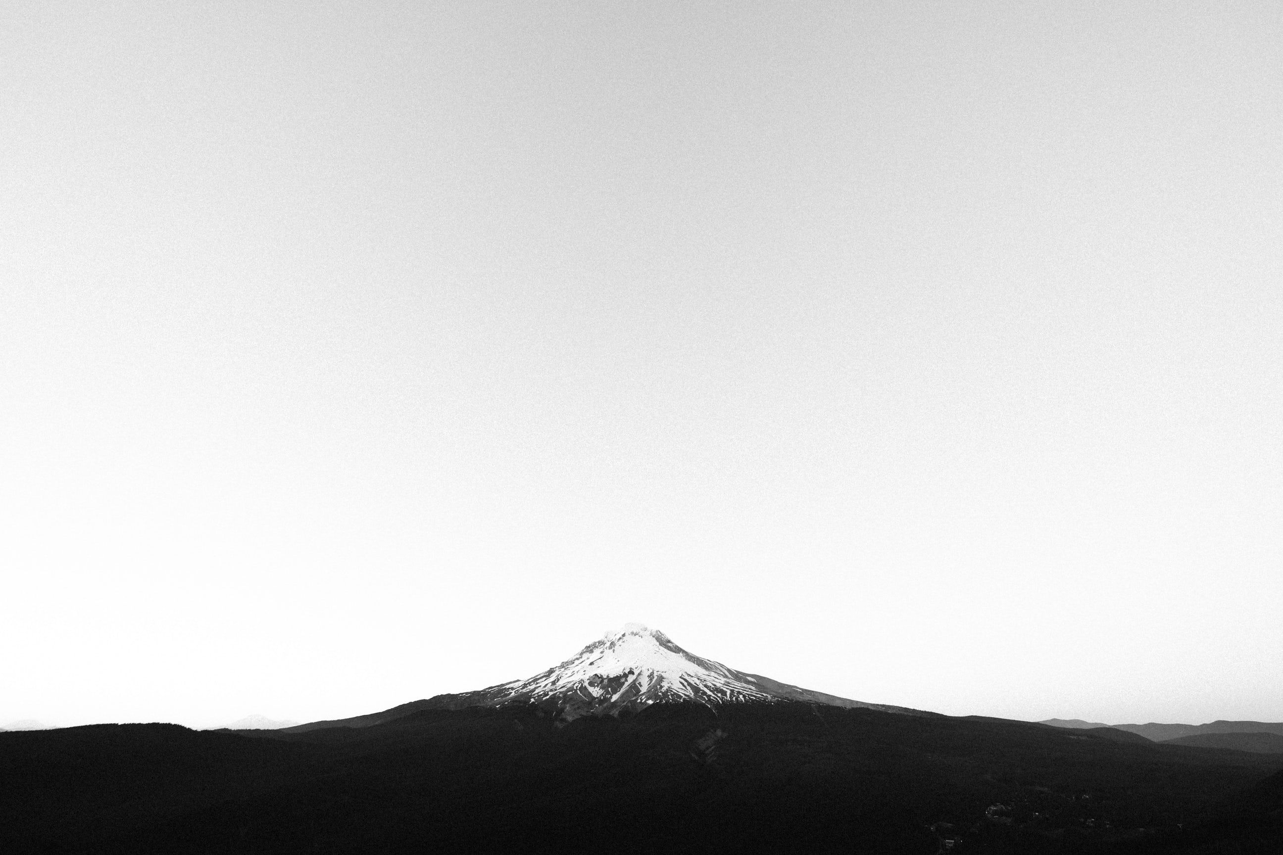 A snowy mountain peak rising up above the desolate landscape. Black and white wallpaper, White wallpaper, Black and white picture