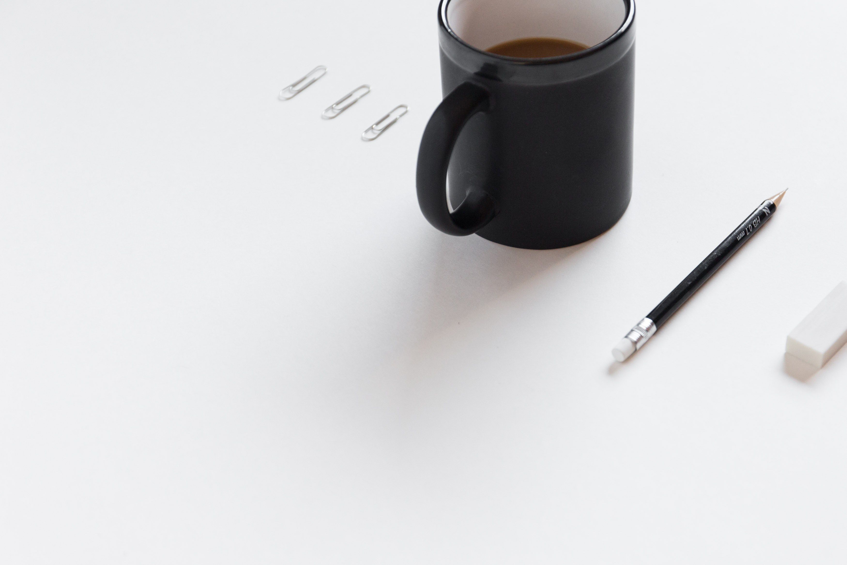 Wallpaper / a pencil an eraser and paper clips next to a cup of coffee, office supplies and coffee 4k wallpaper