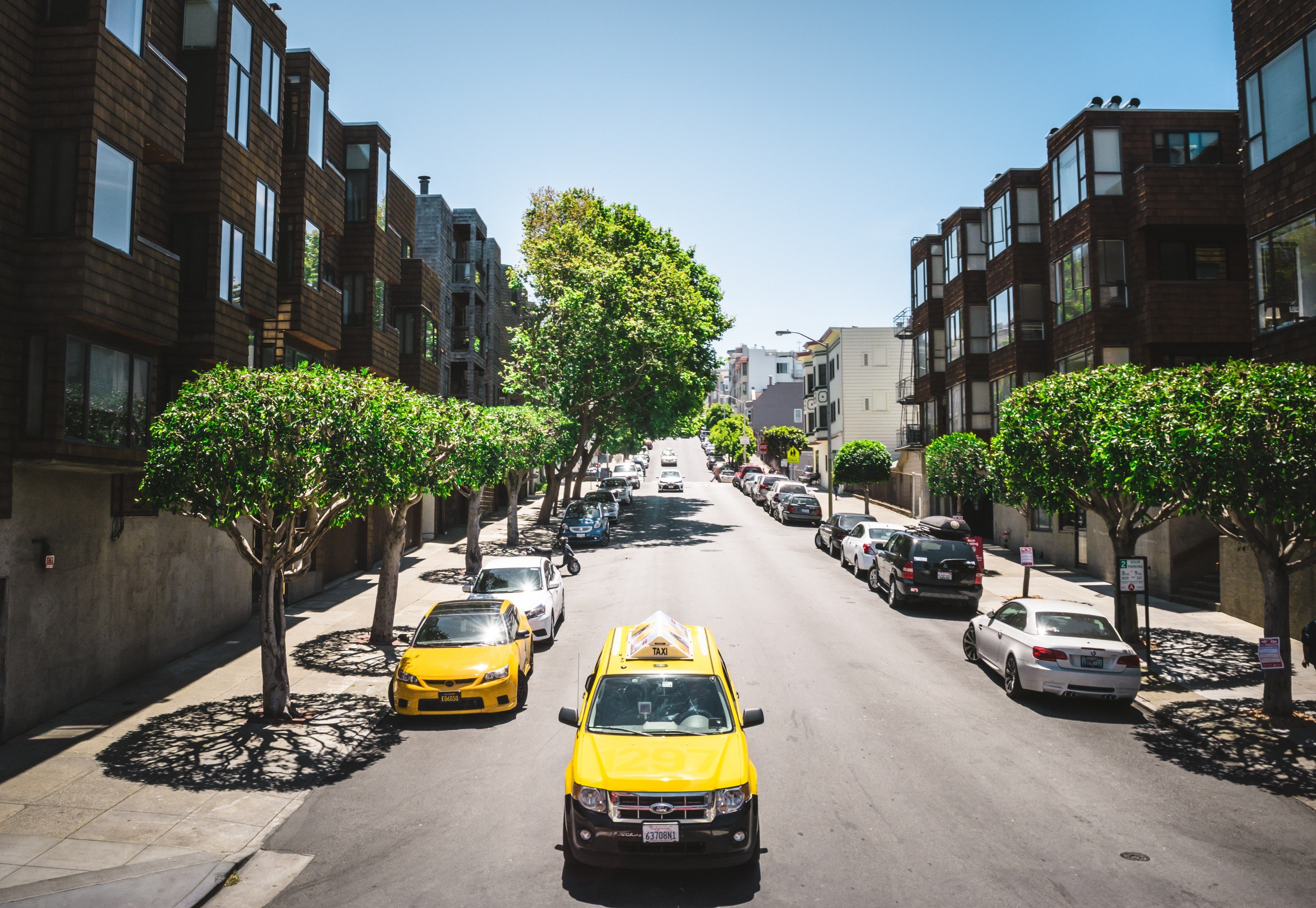Wallpaper / yellow ford taxi car on a sunny urban avenue with parked cars on both sides, yellow ford taxi car on a sunny avenue 4k wallpaper