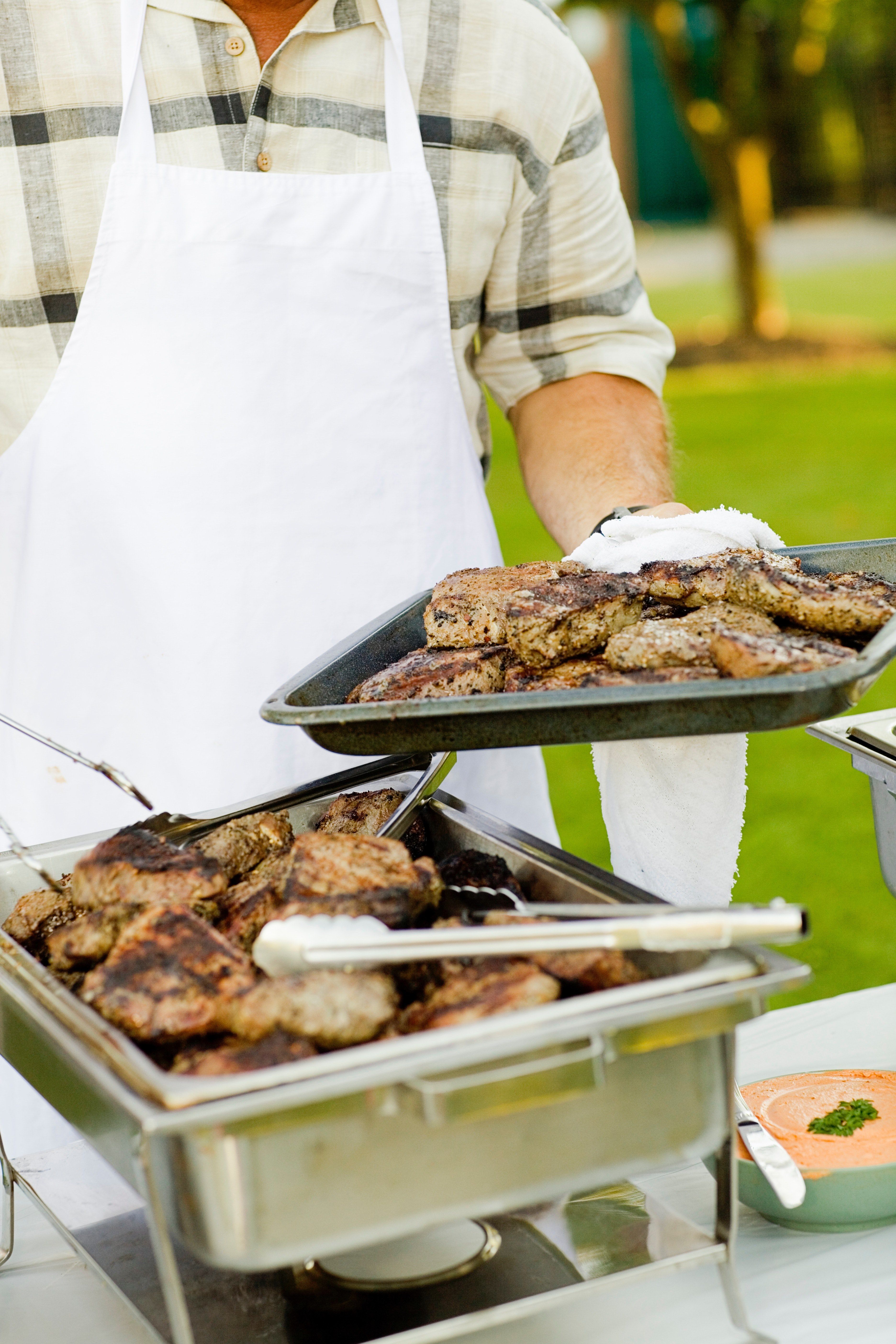 Wallpaper / a man wearing a white apron setting up a catering table of bbq food, cooking meat 4k wallpaper