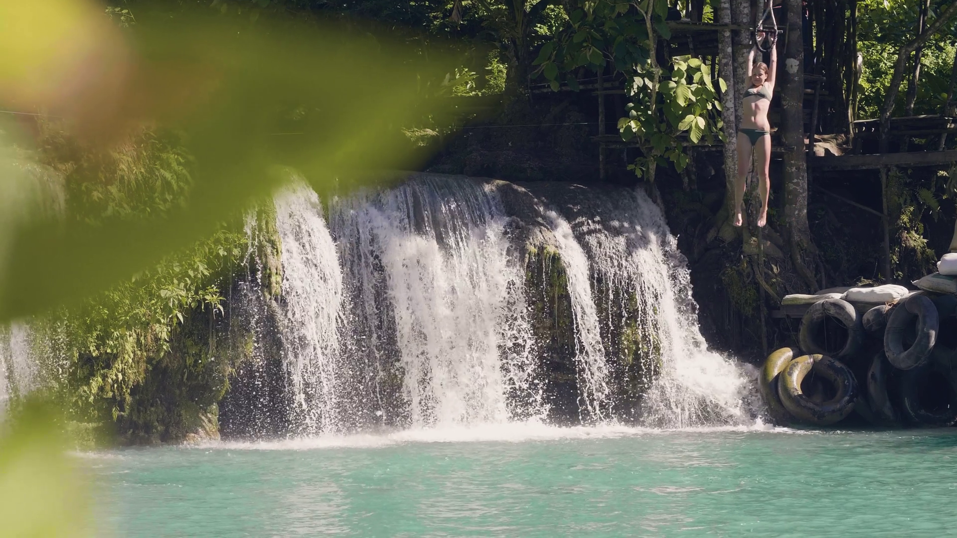 Young woman jumping in mountain lake from rope and splashing waterfall on background. Slow motion. Happy woman jumping in waterfall lake from rope and stick. Extreme rest on summer vacation. Stock Video