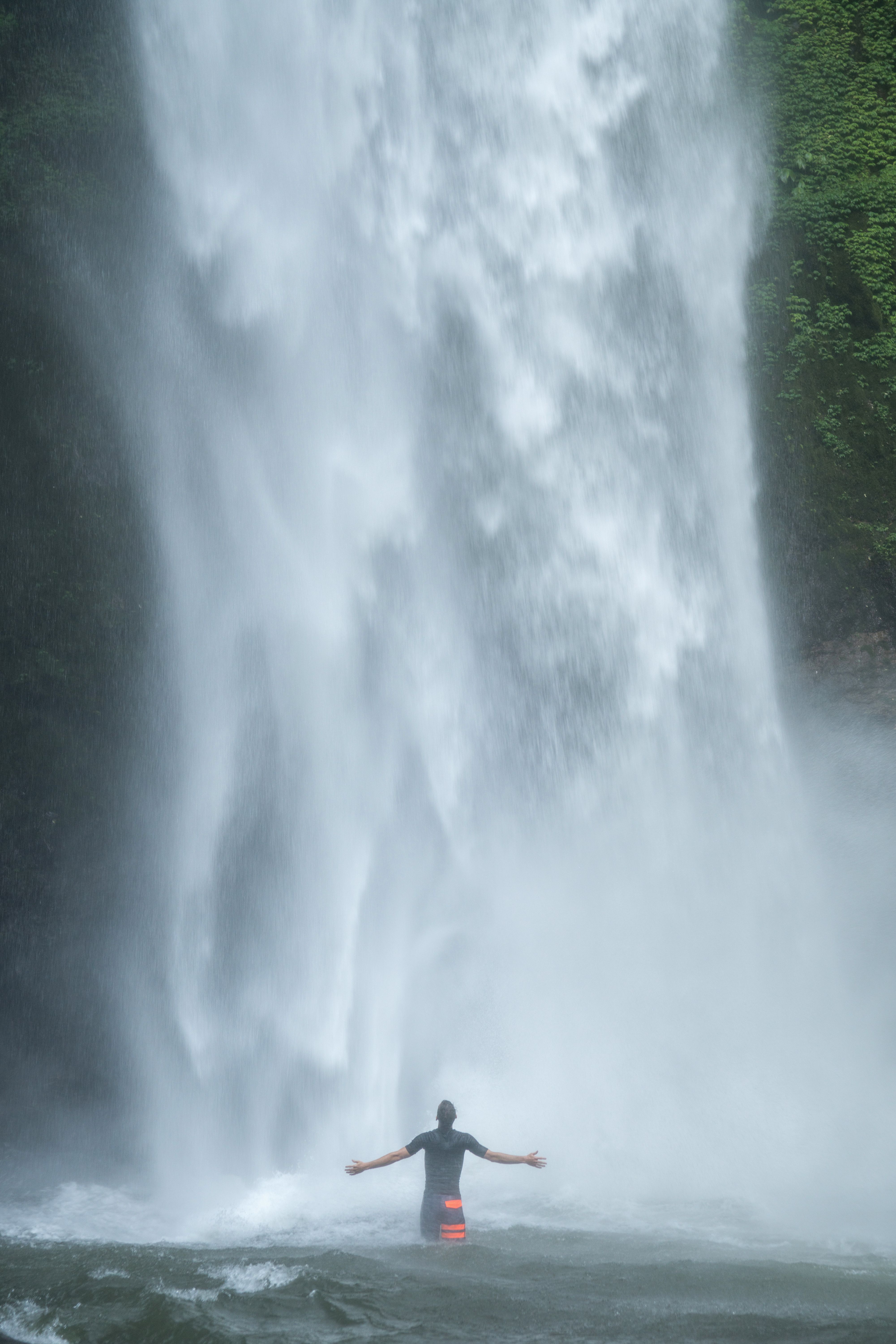 Man bathing in waterfall lake with arms outstretched · Free
