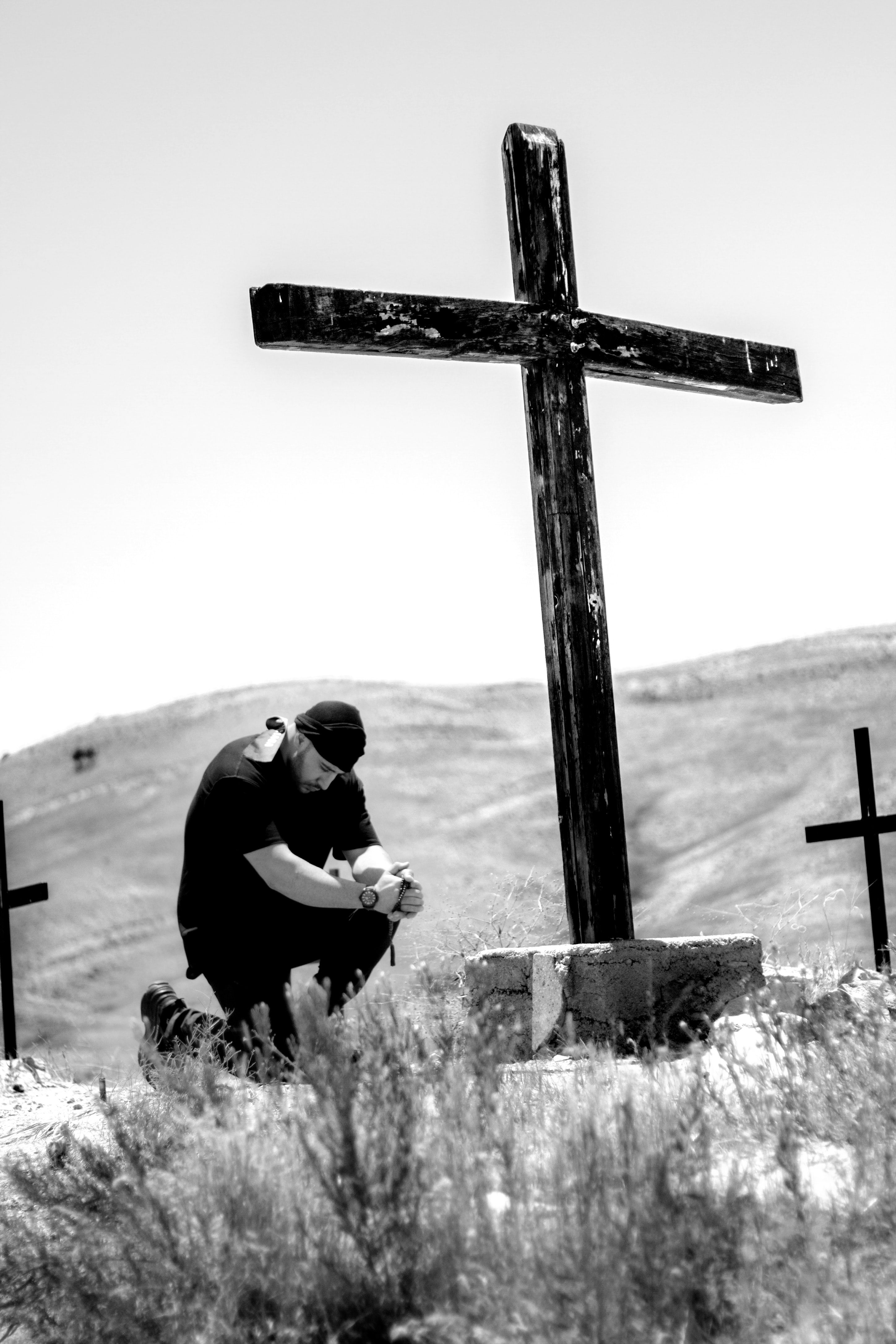 man kneeling in front of wooden cross photo