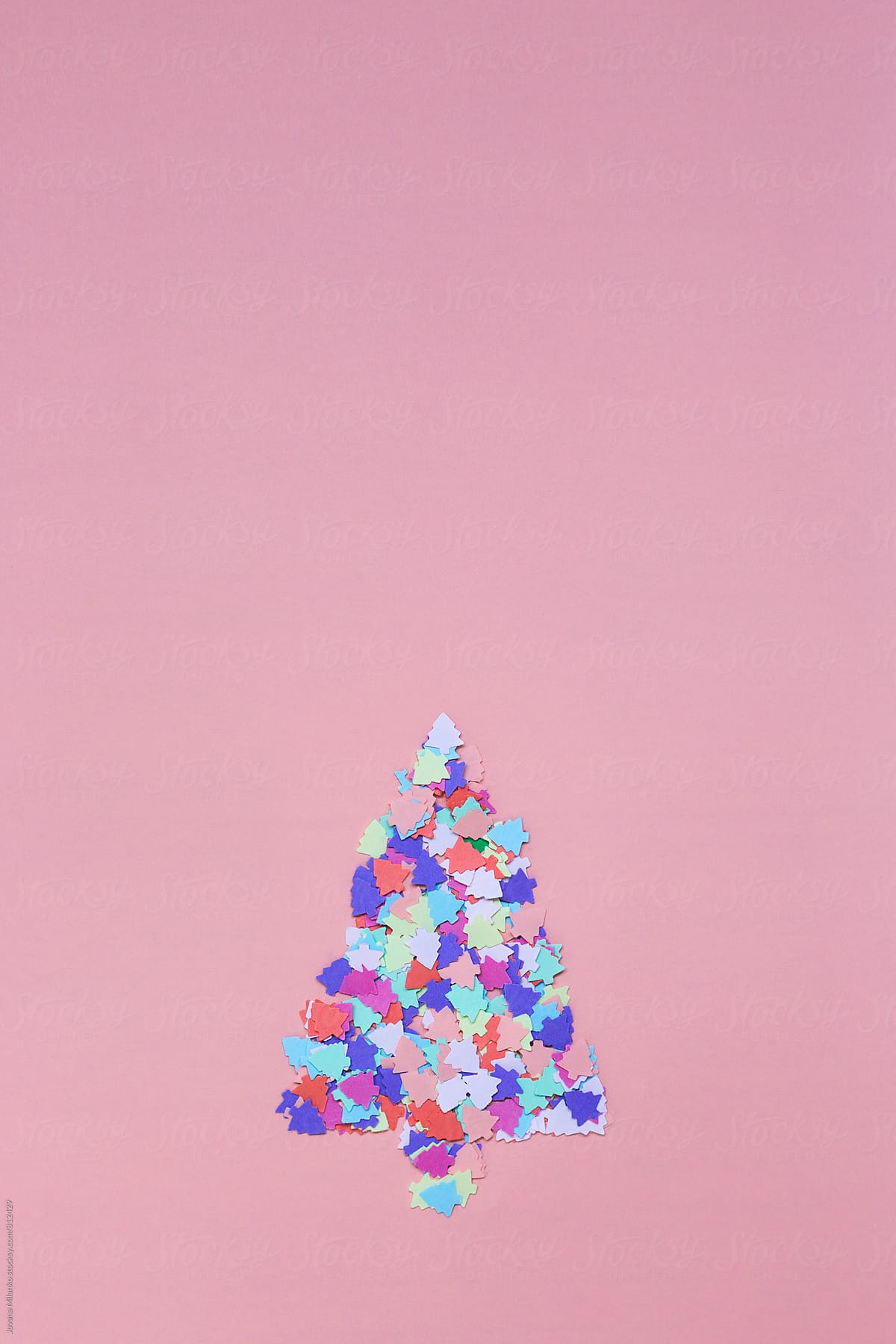 Confetti cut in a shape of a Christmas tree making a bigger Christmas tree on a pink background