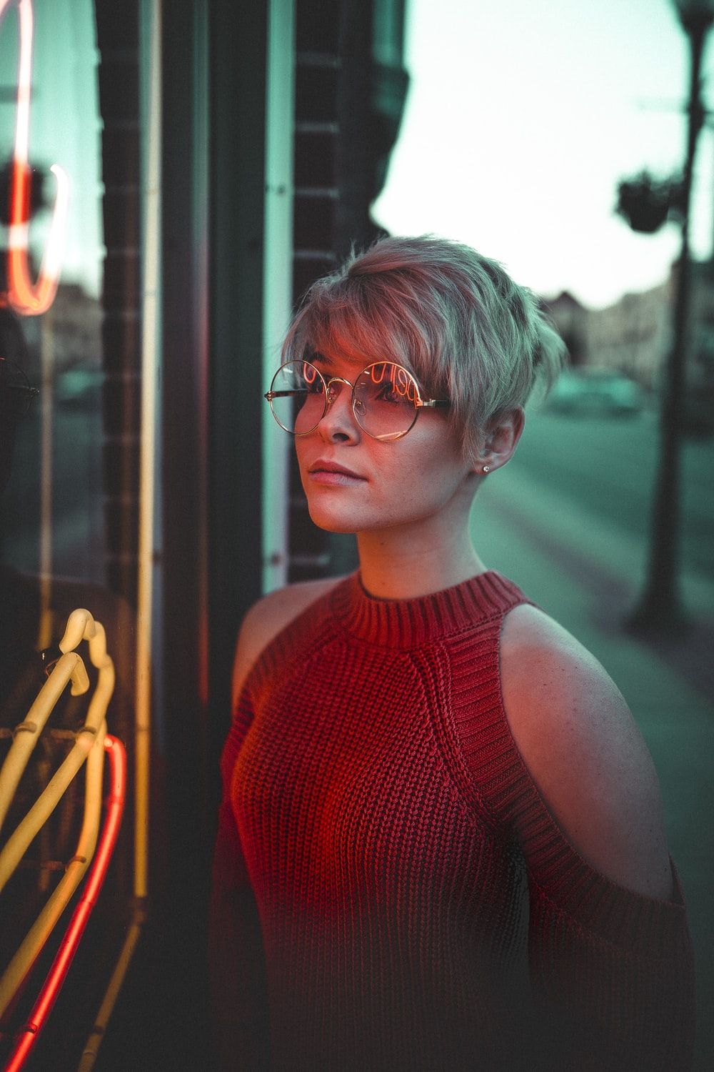 woman with eyeglasses looking at glass panel with neon signage photo