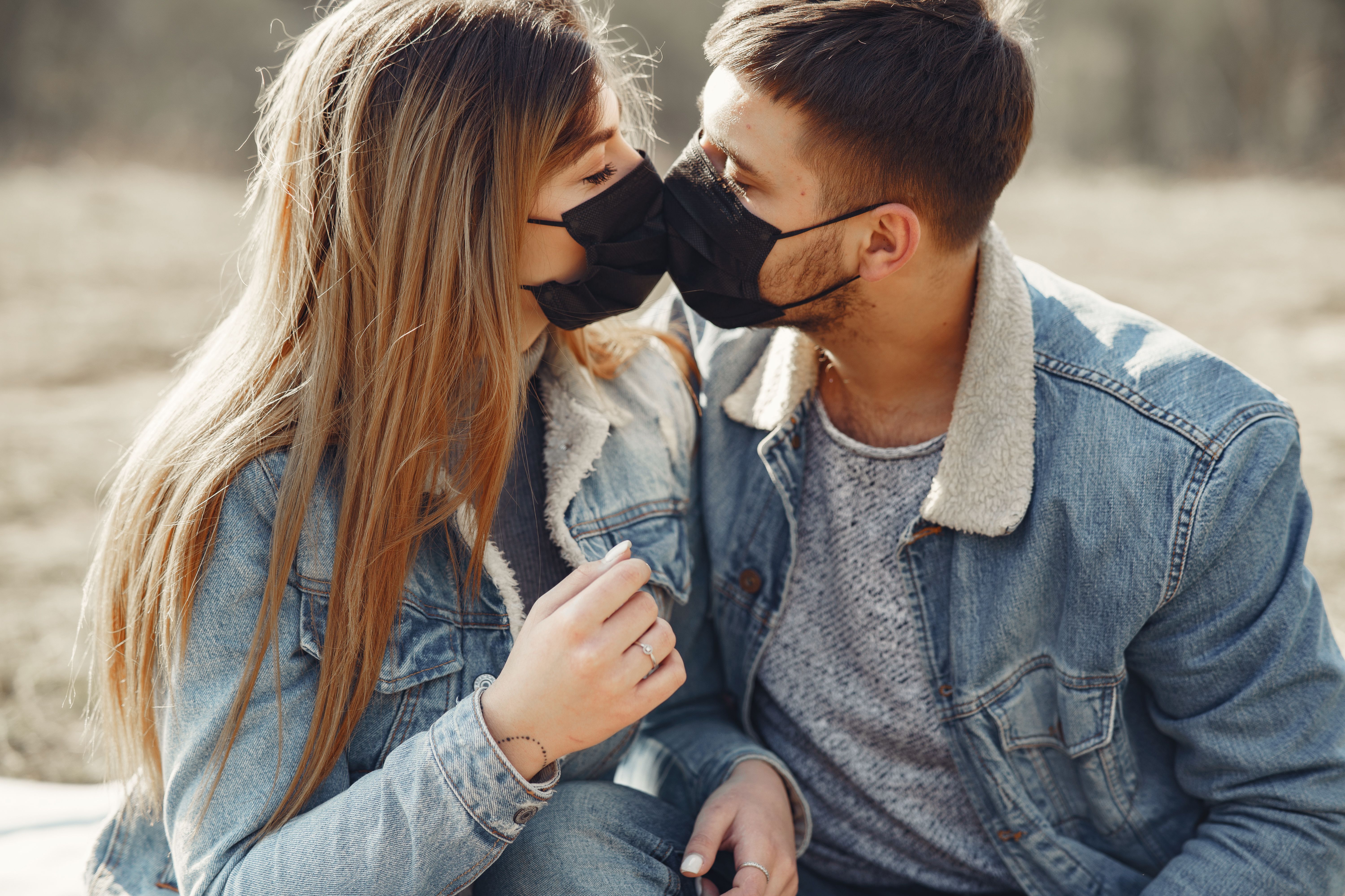 Loving young couple kissing while wearing black medical masks · Free