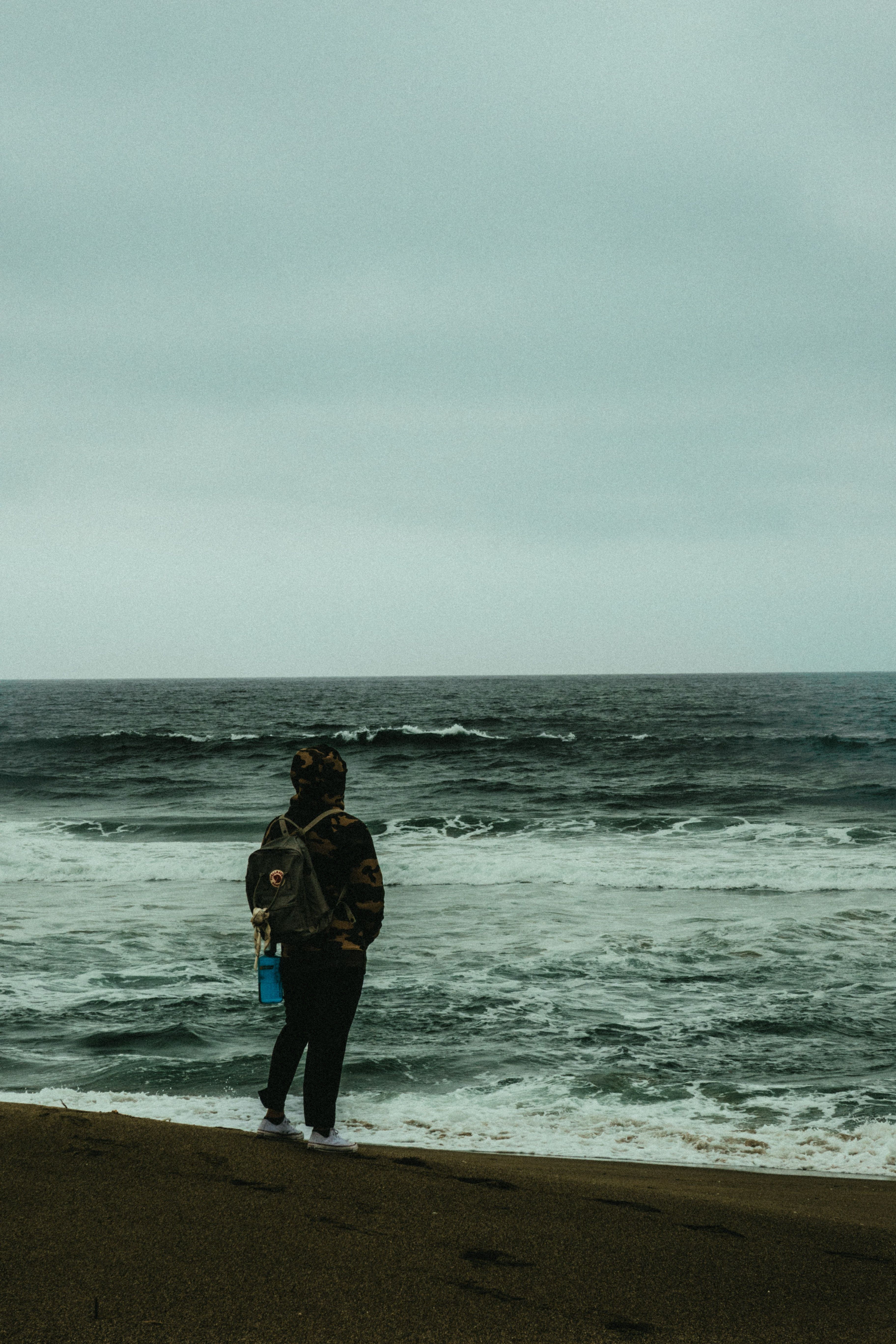 Photo of Person Carrying Backpack Standing Alone on the Beach Overlooking the Horizon · Free