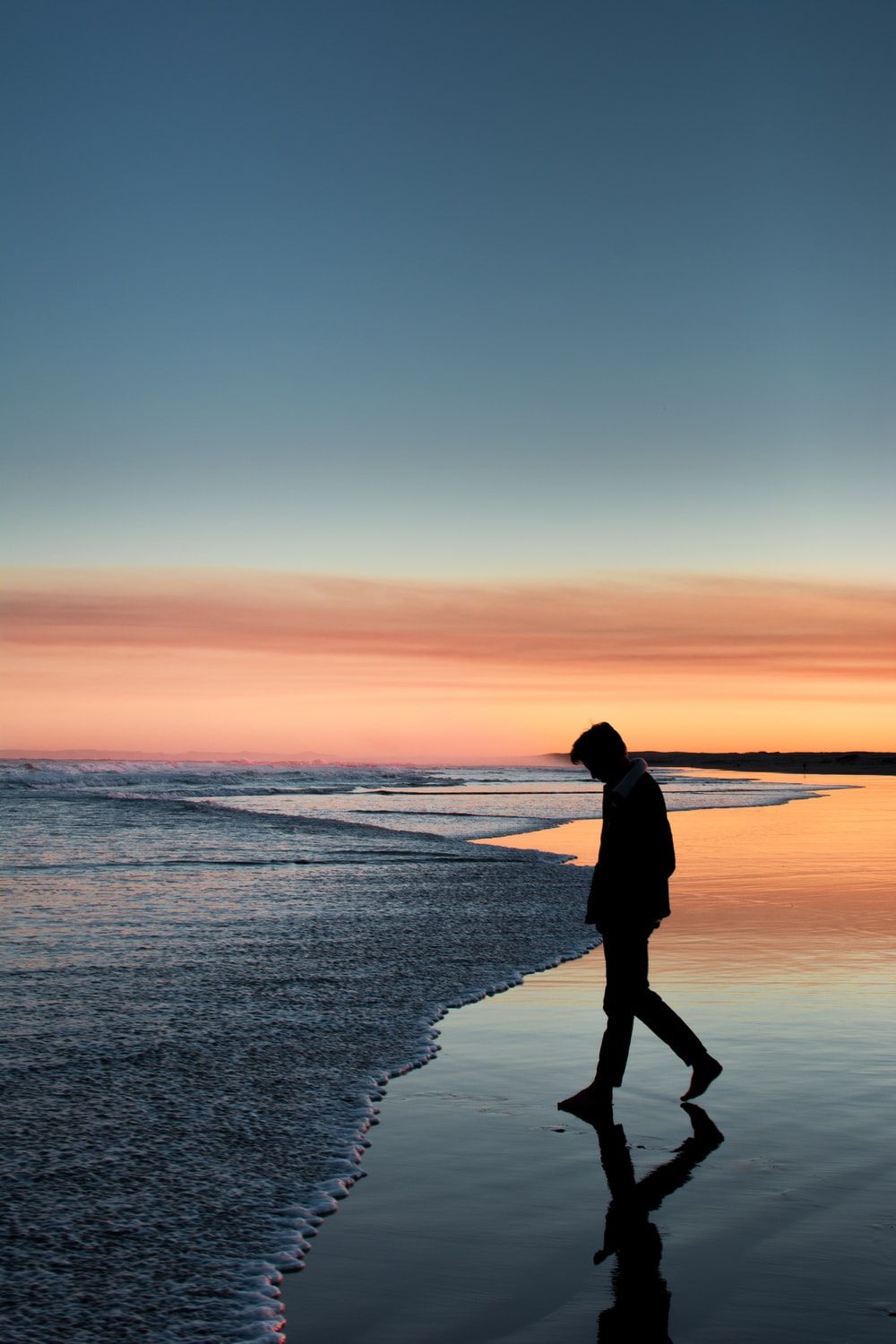 silhouette of person walking on beach during sunset photo