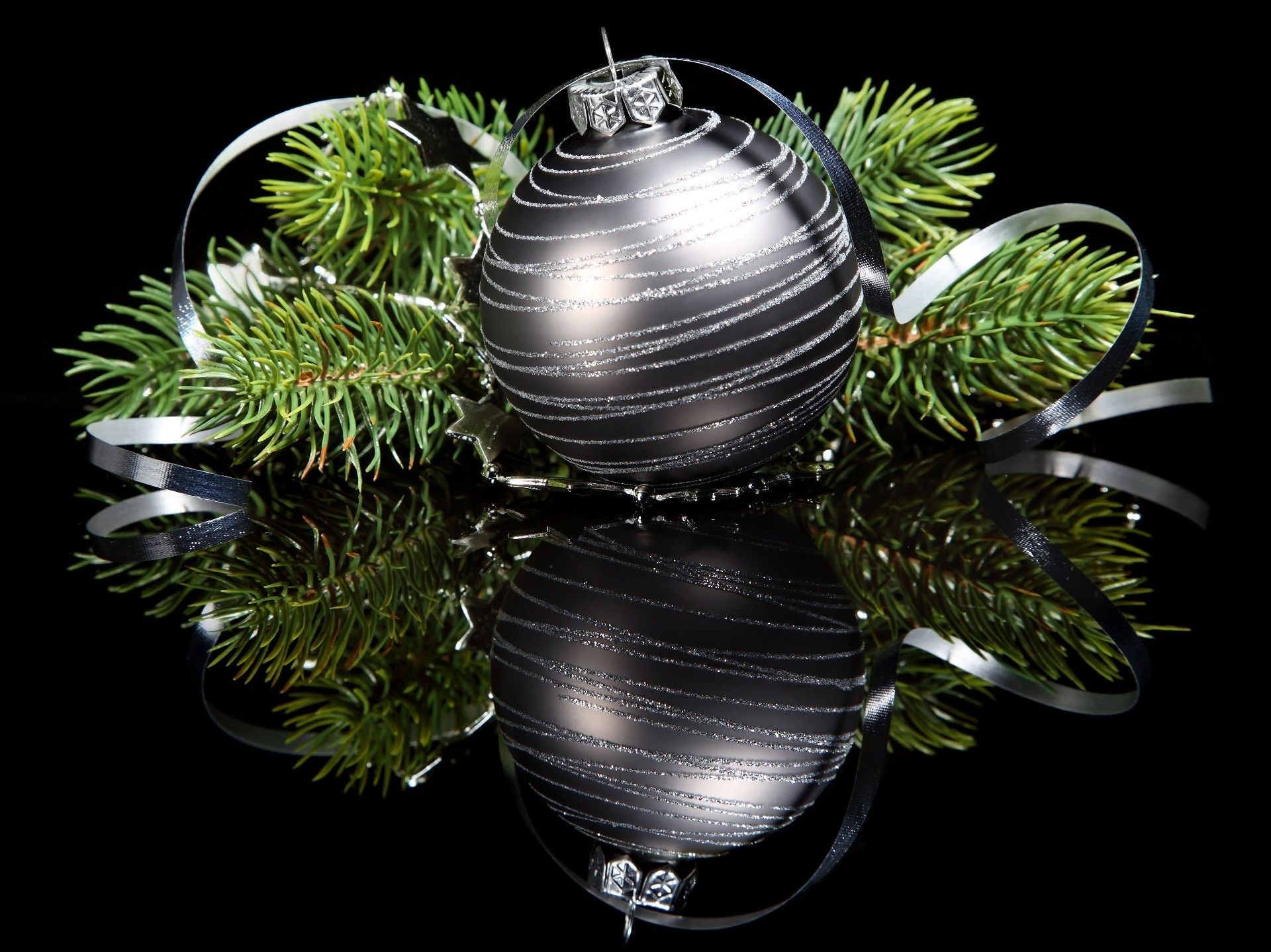 Silver Christmas ball with green branches on a black mirror
