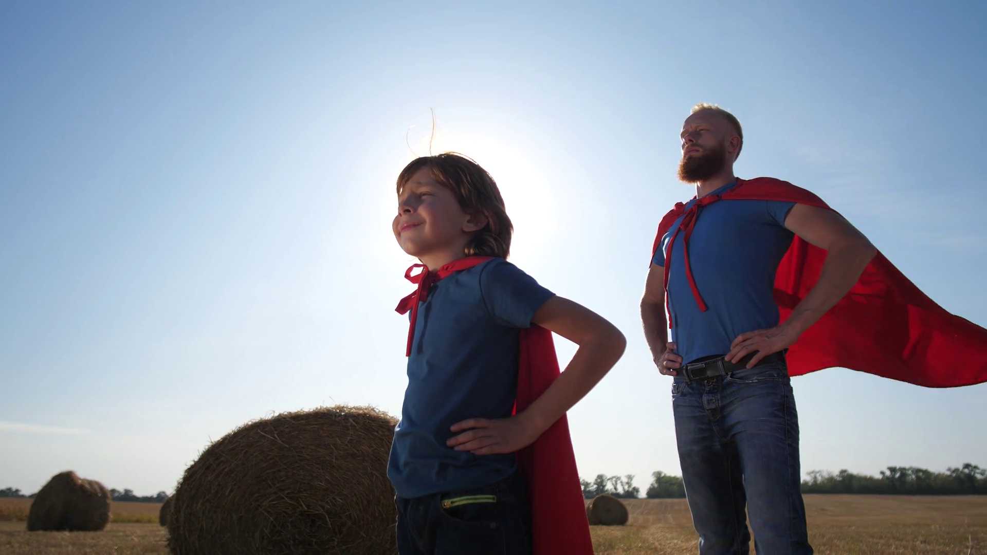 Confident father and son in superhero pose standing with hands on hips and looking into distance during sunset. Redhead man and child stretching forward clenched fist and saying superhero's motto Stock Video